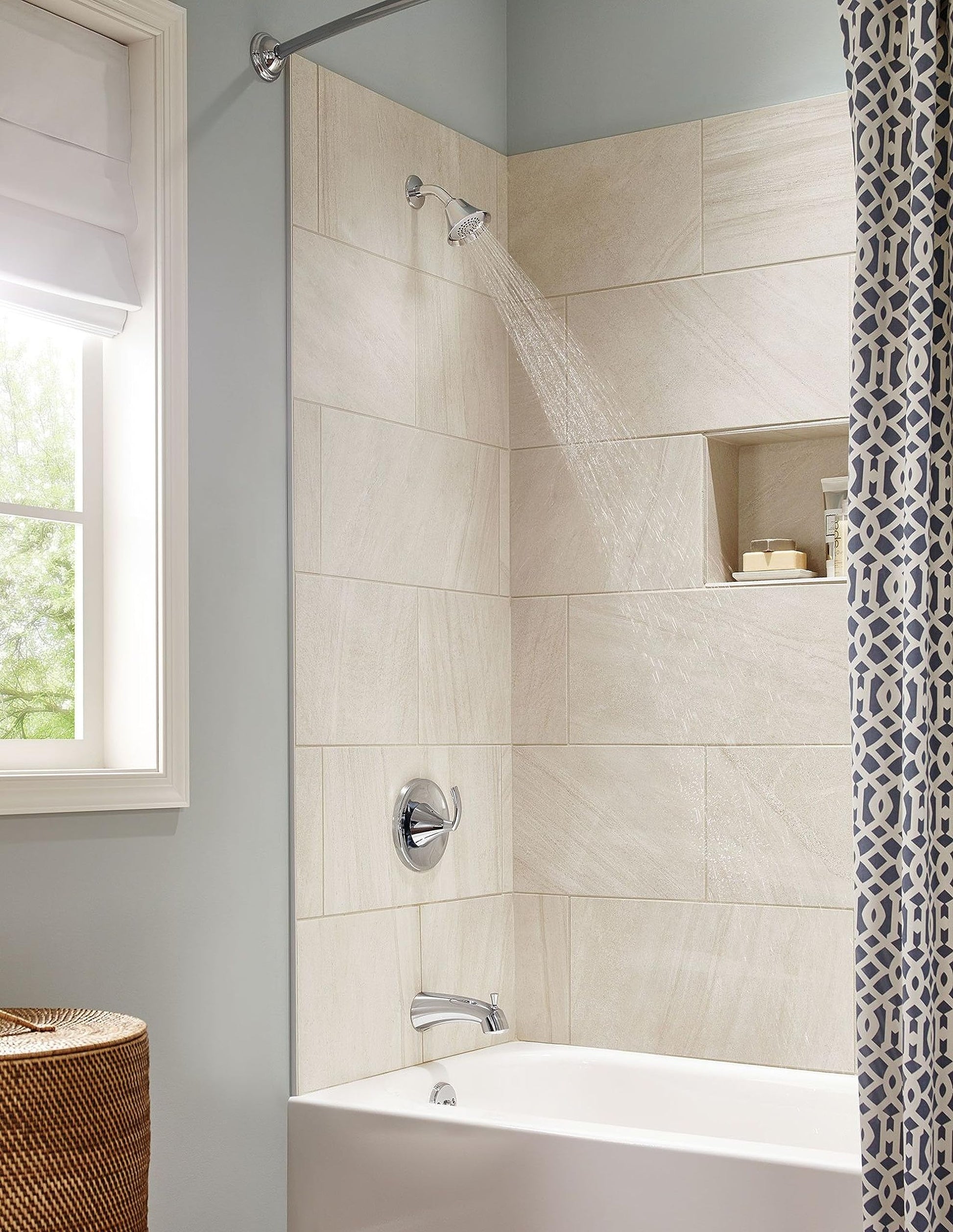 Brushed nickel single-handle shower valve trim with round trim plate and matching showerhead mounted above bathtub.