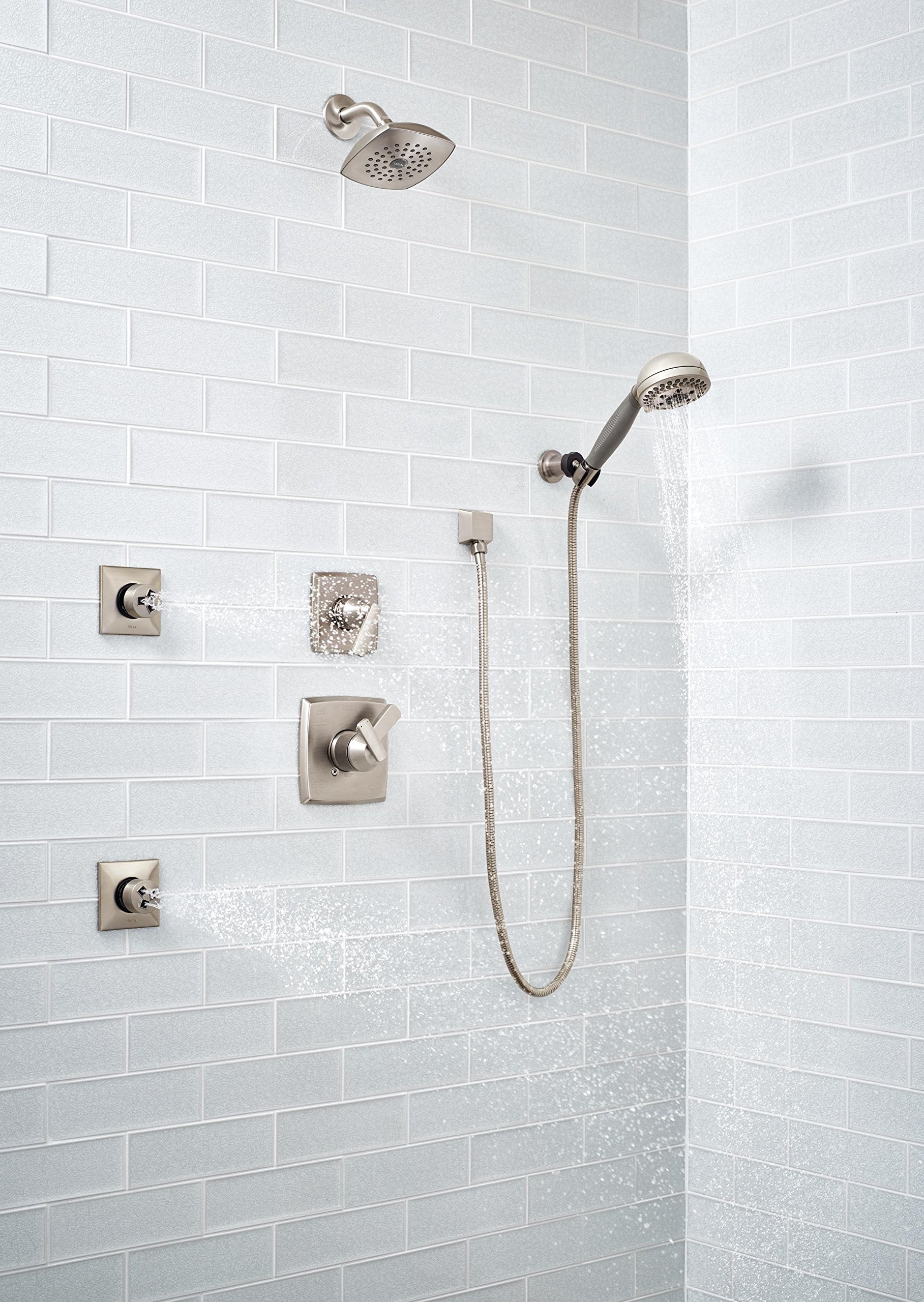 Square stainless steel wall elbow connector for hand shower mounted on white subway tile.