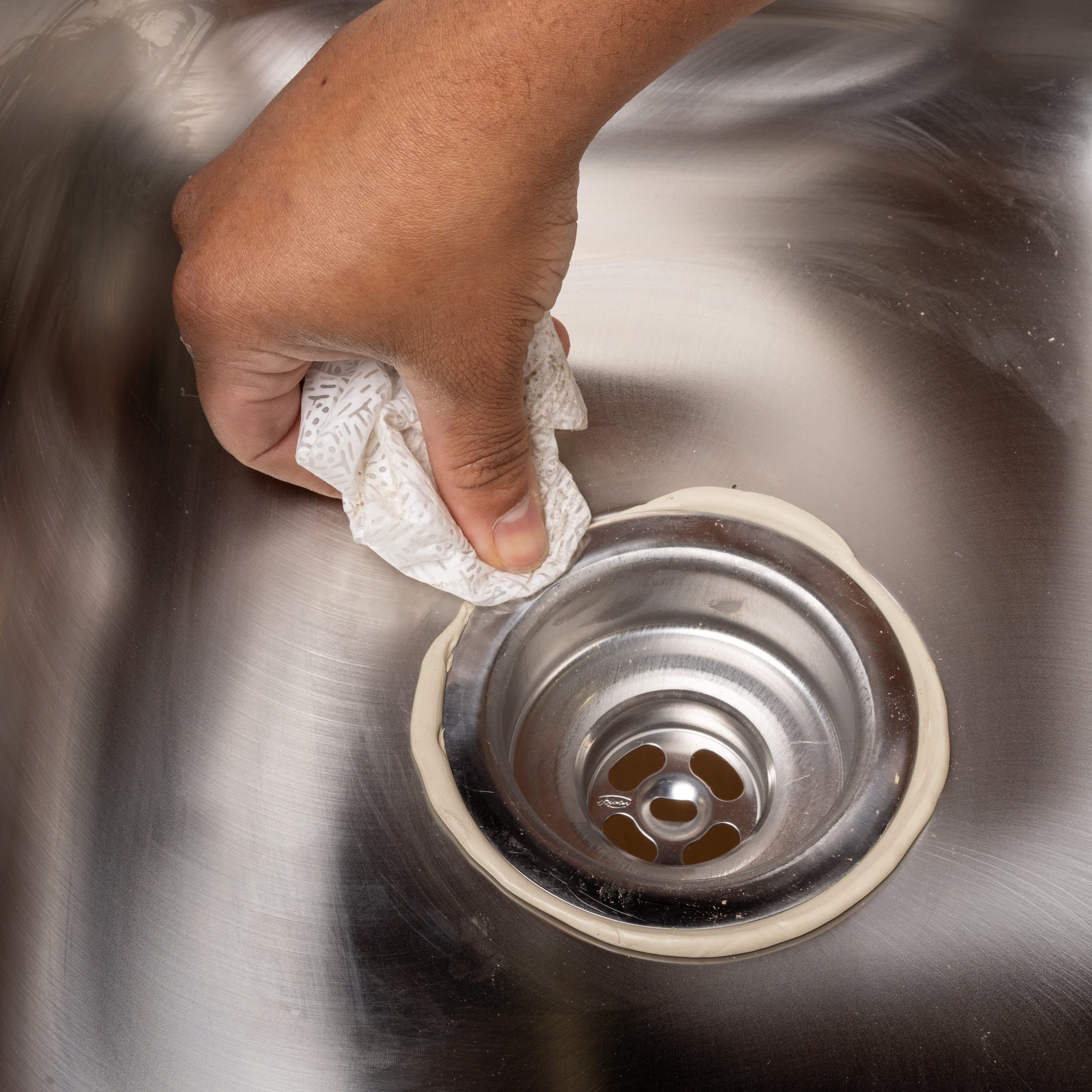 Tan-colored plumber's putty being applied around a sink drain opening with a hand holding the material.