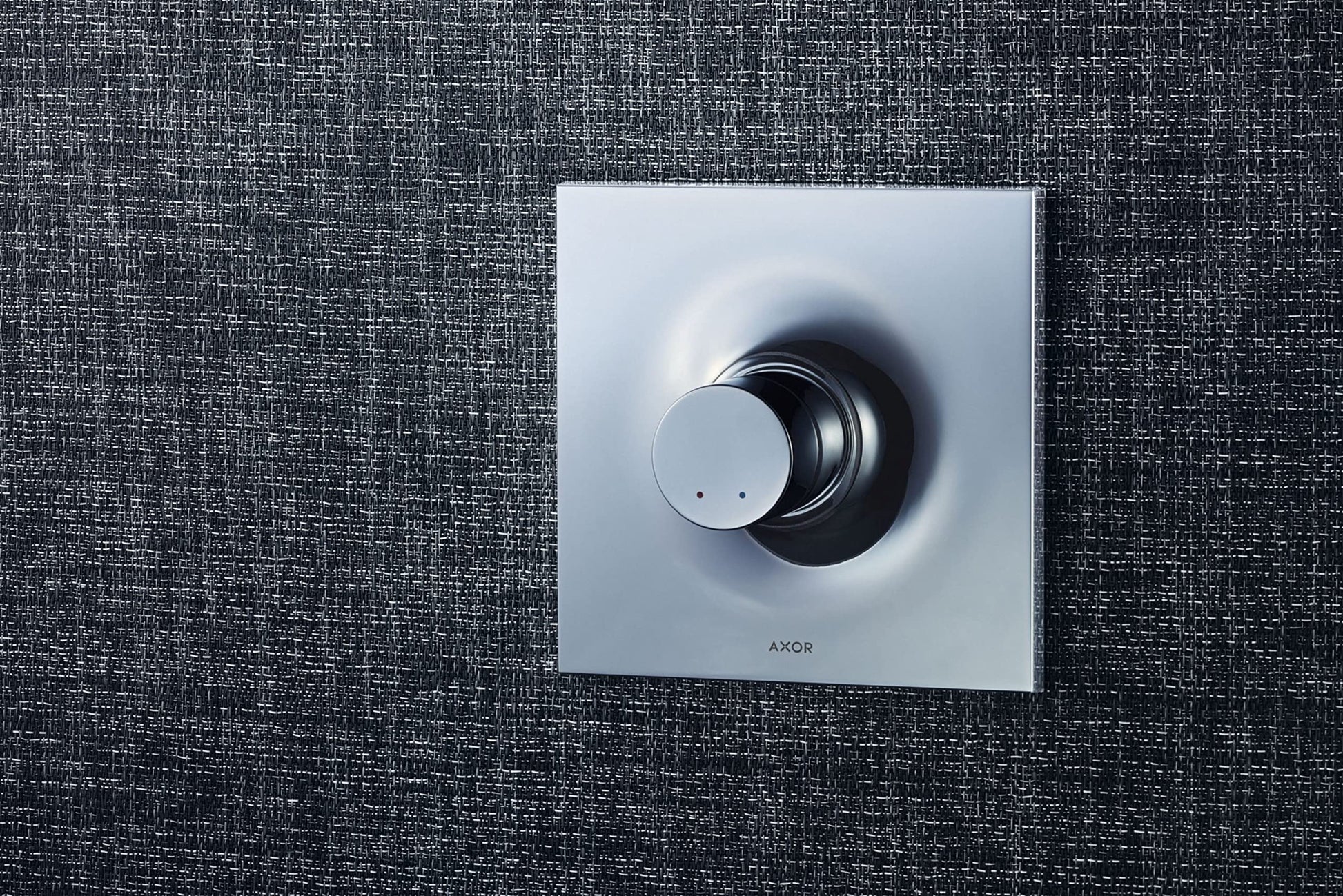 Chrome AXOR Massaud thermostatic trim with square escutcheon and circular dial control on dark textured wall.