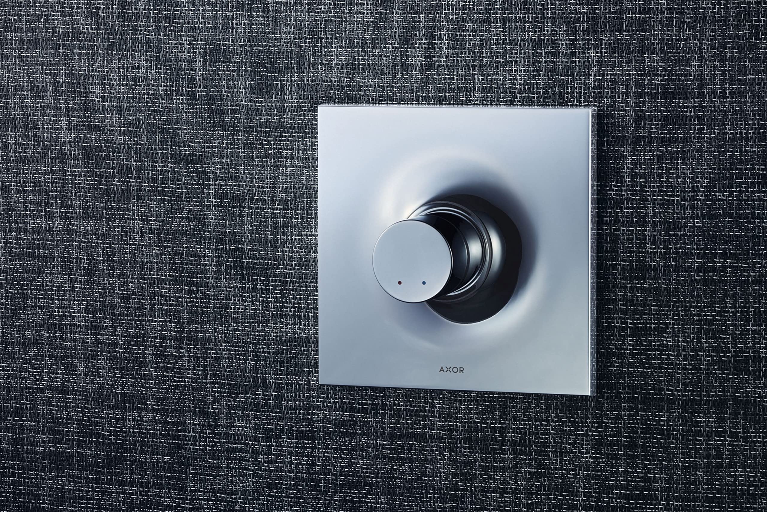 Chrome AXOR Massaud thermostatic trim with square escutcheon and circular dial control on dark textured wall.