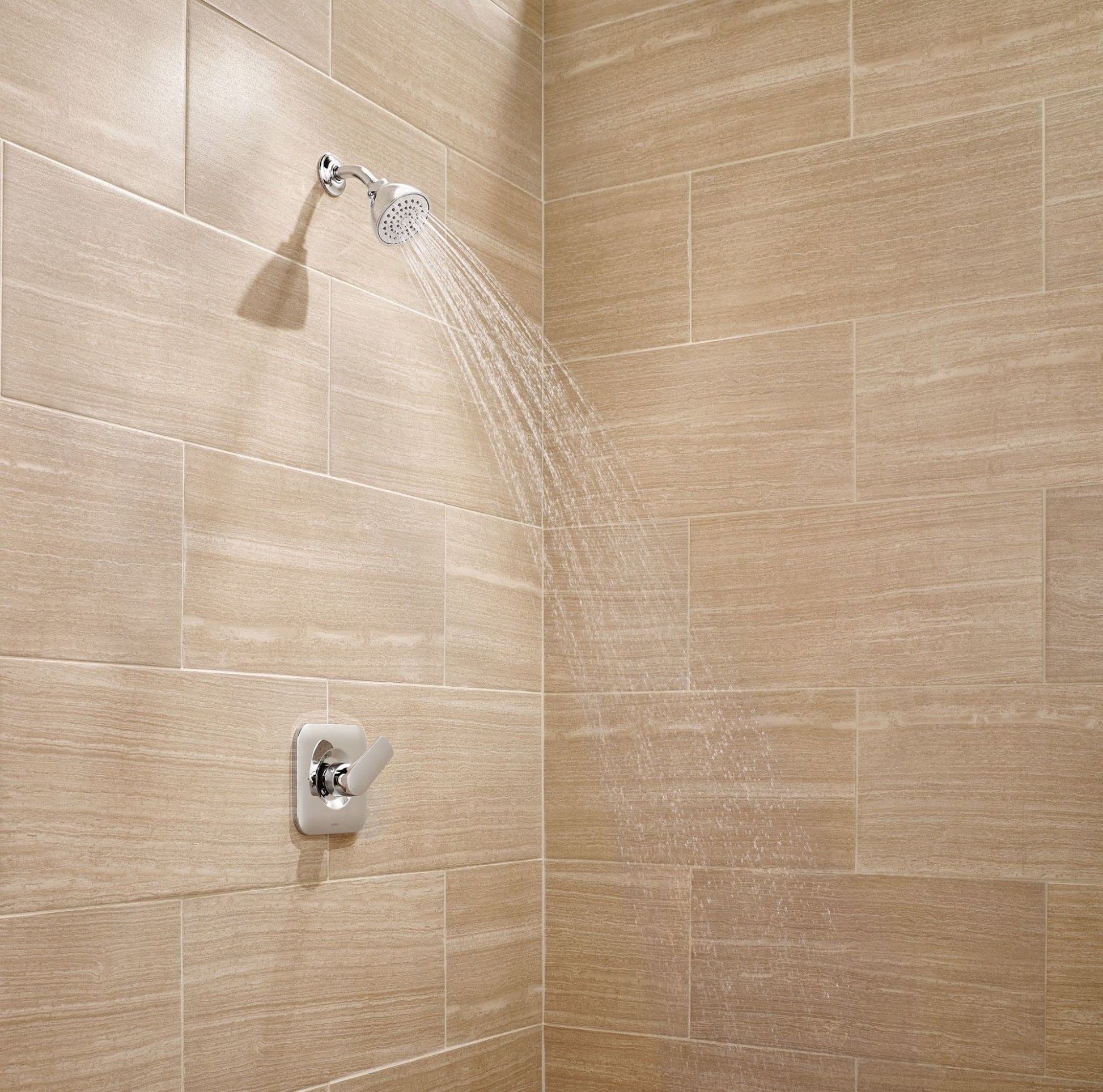 Chrome shower trim with round showerhead and valve control mounted on beige tile wall.