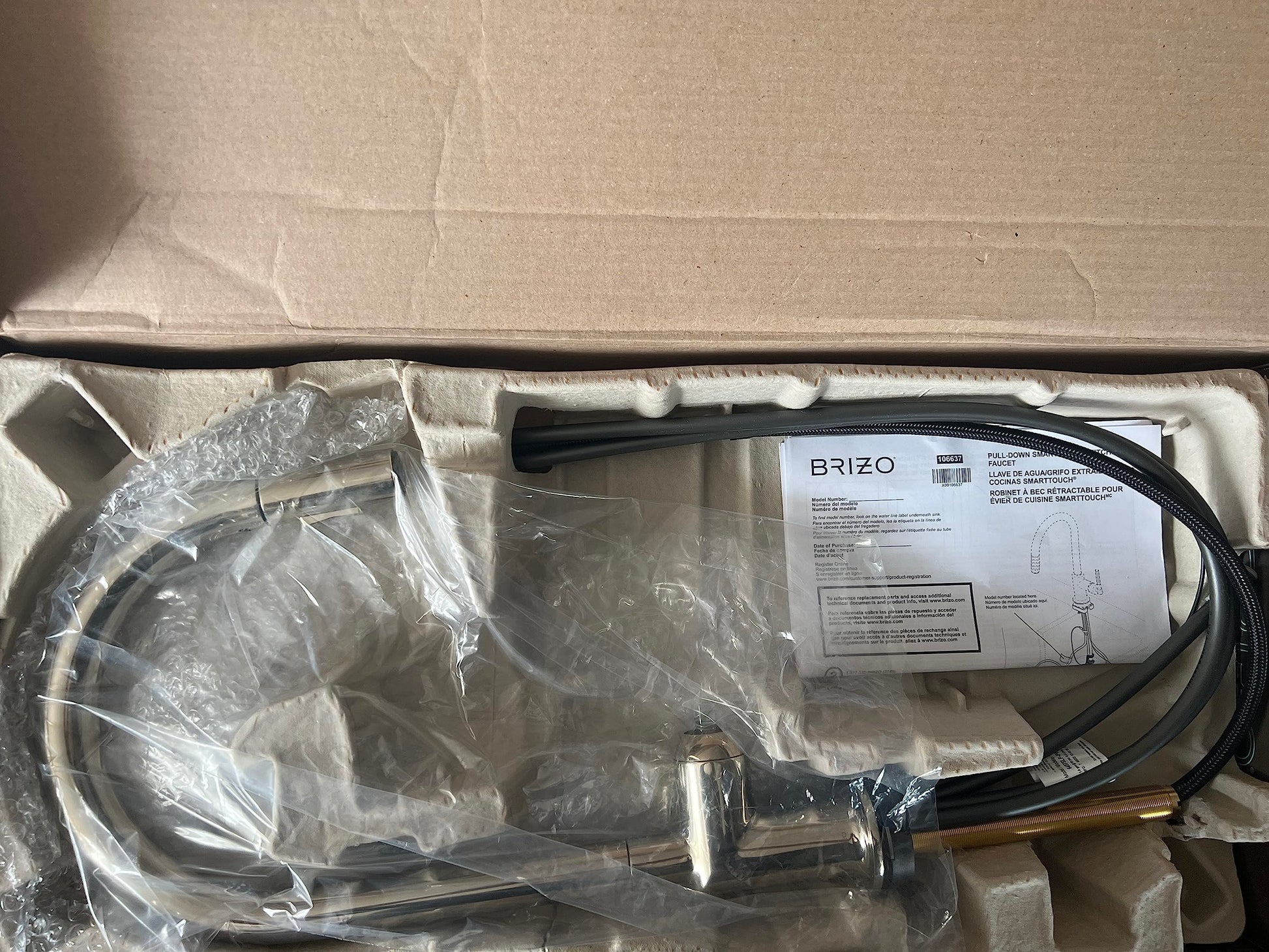 Polished nickel pull-down kitchen faucet with arc spout and black hose, shown unboxed with instruction manual and packaging m
