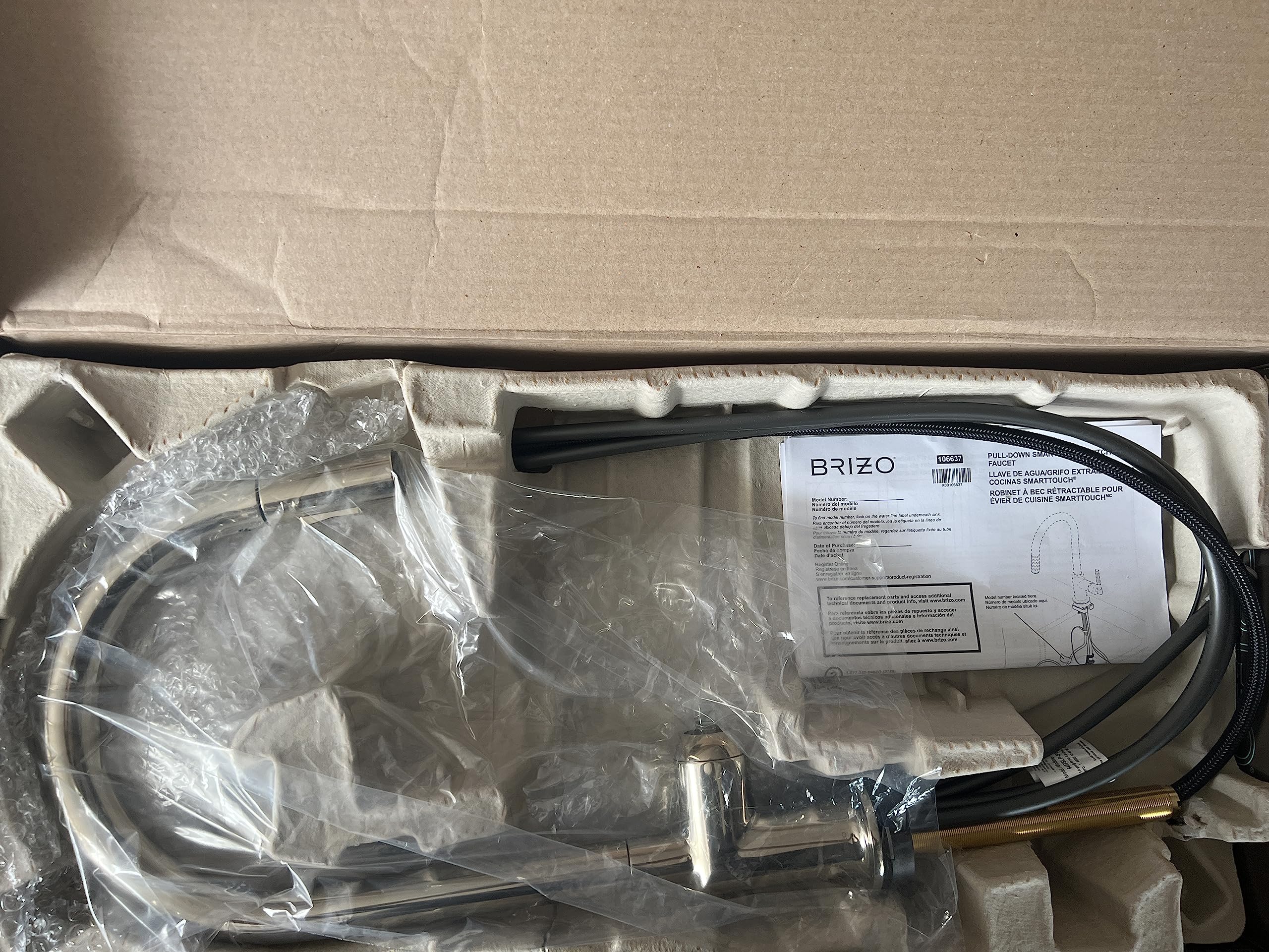Polished nickel pull-down kitchen faucet with arc spout and black hose, shown unboxed with instruction manual and packaging m