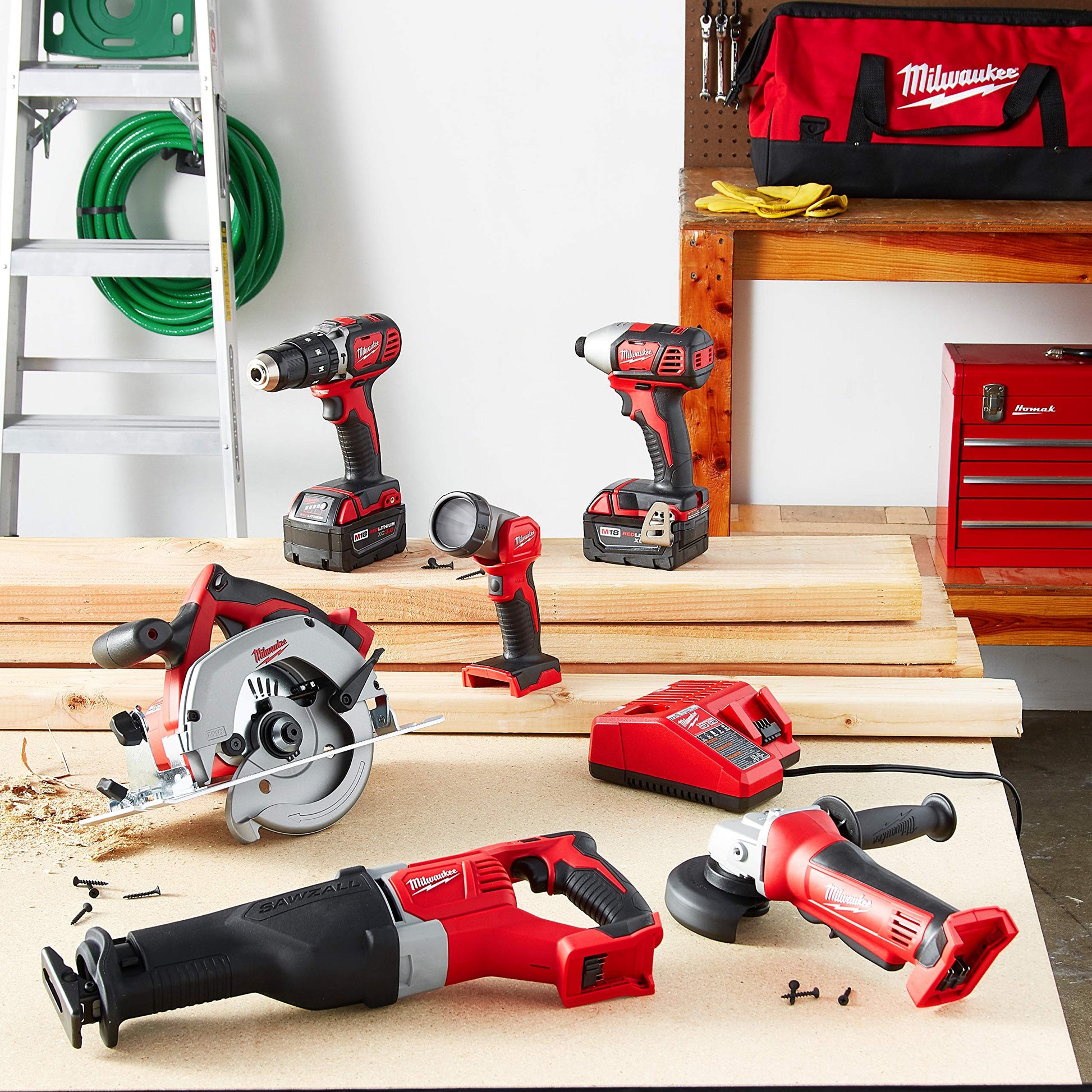 Milwaukee M18 cordless combo kit with six red and black tools, batteries, charger, and carrying bag displayed in workshop set