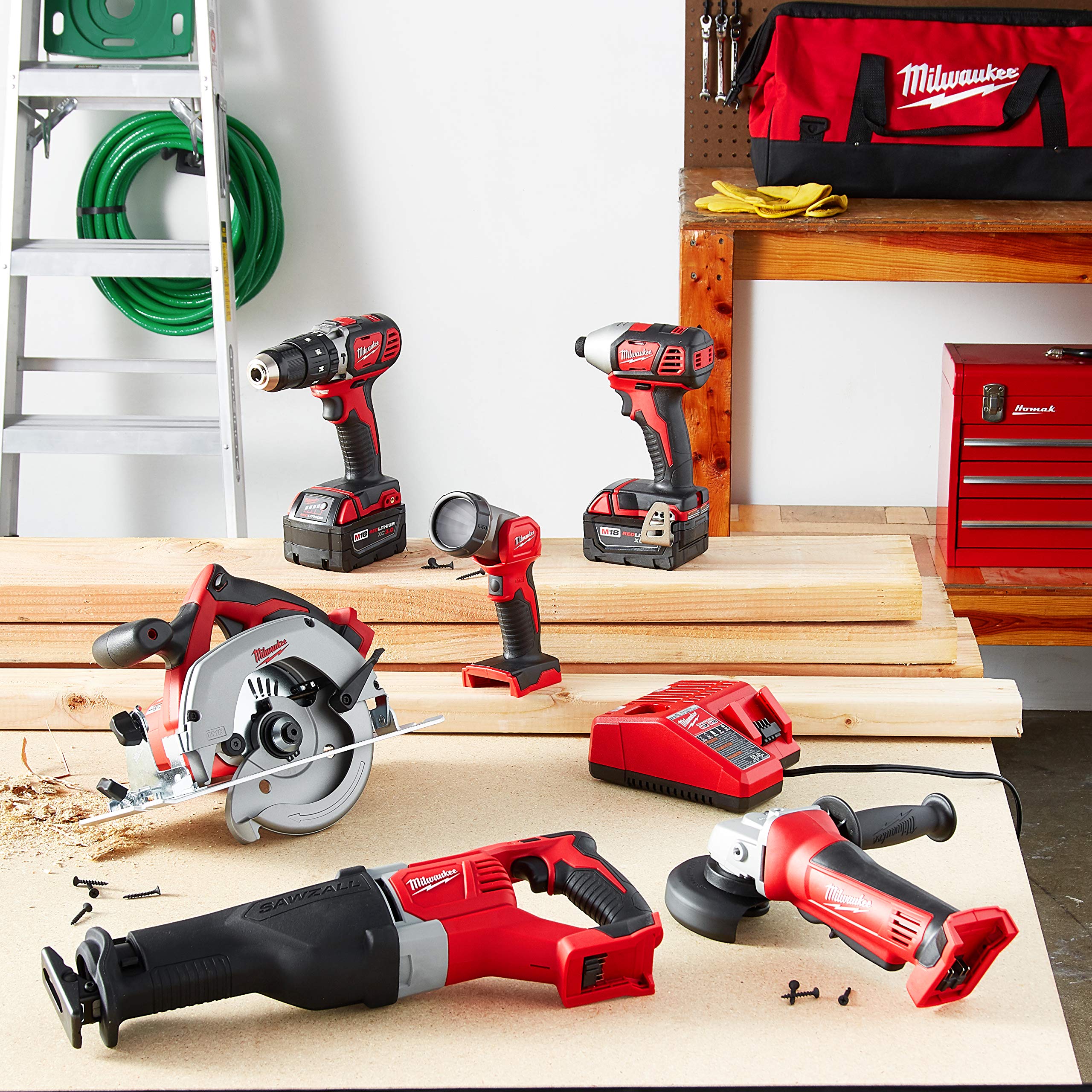 Milwaukee M18 cordless combo kit with six red and black tools, batteries, charger, and carrying bag displayed in workshop set