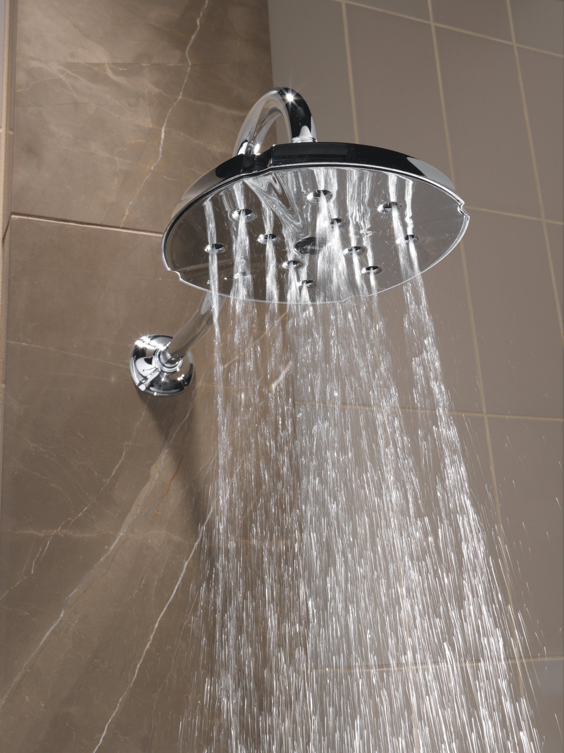 Chrome showerhead with flange mounted on tile wall, dispensing water with control handle visible below.