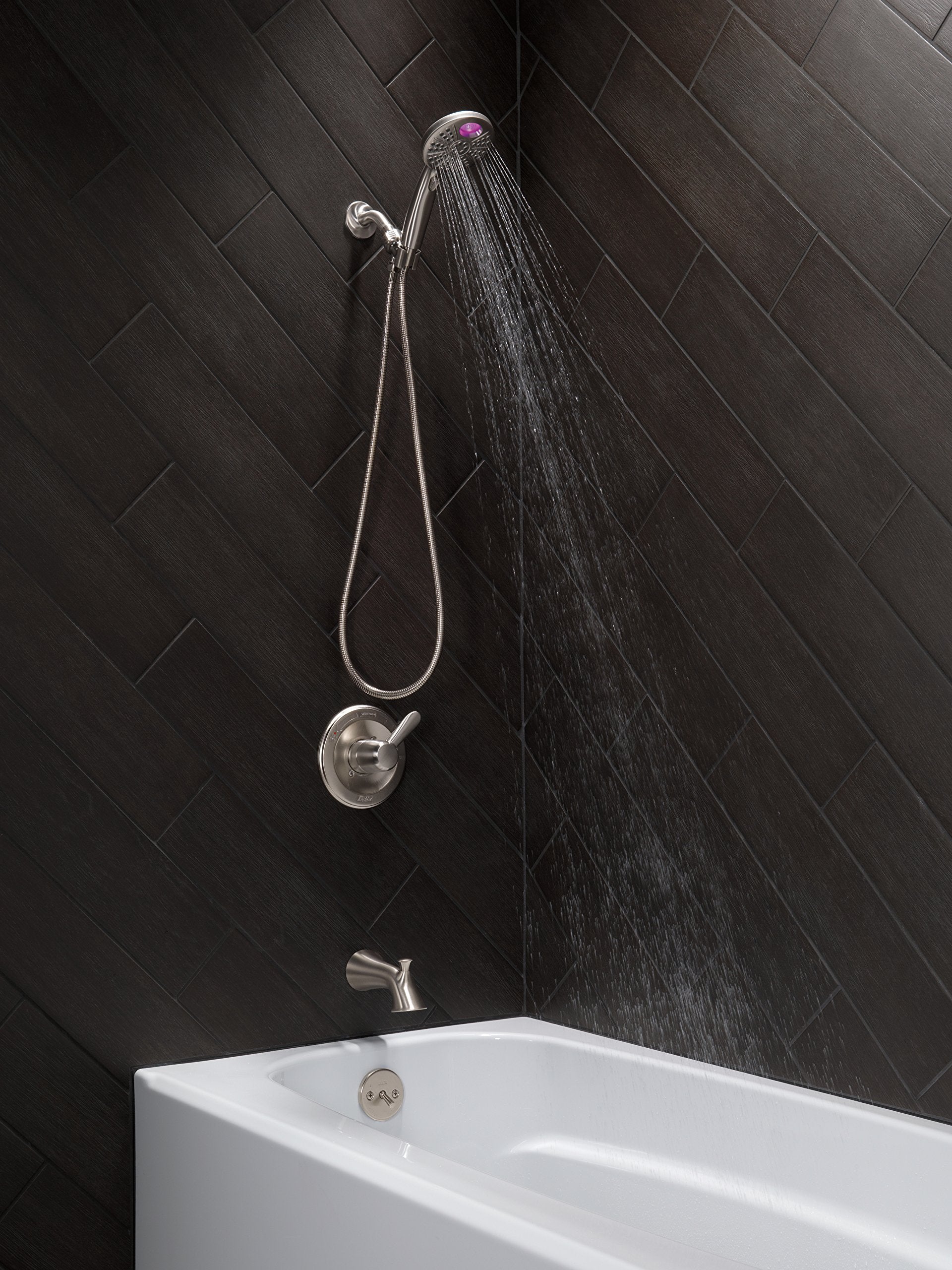 Stainless steel tub spout with pull-up diverter, handheld showerhead, and control valve installed on black tile wall above wh