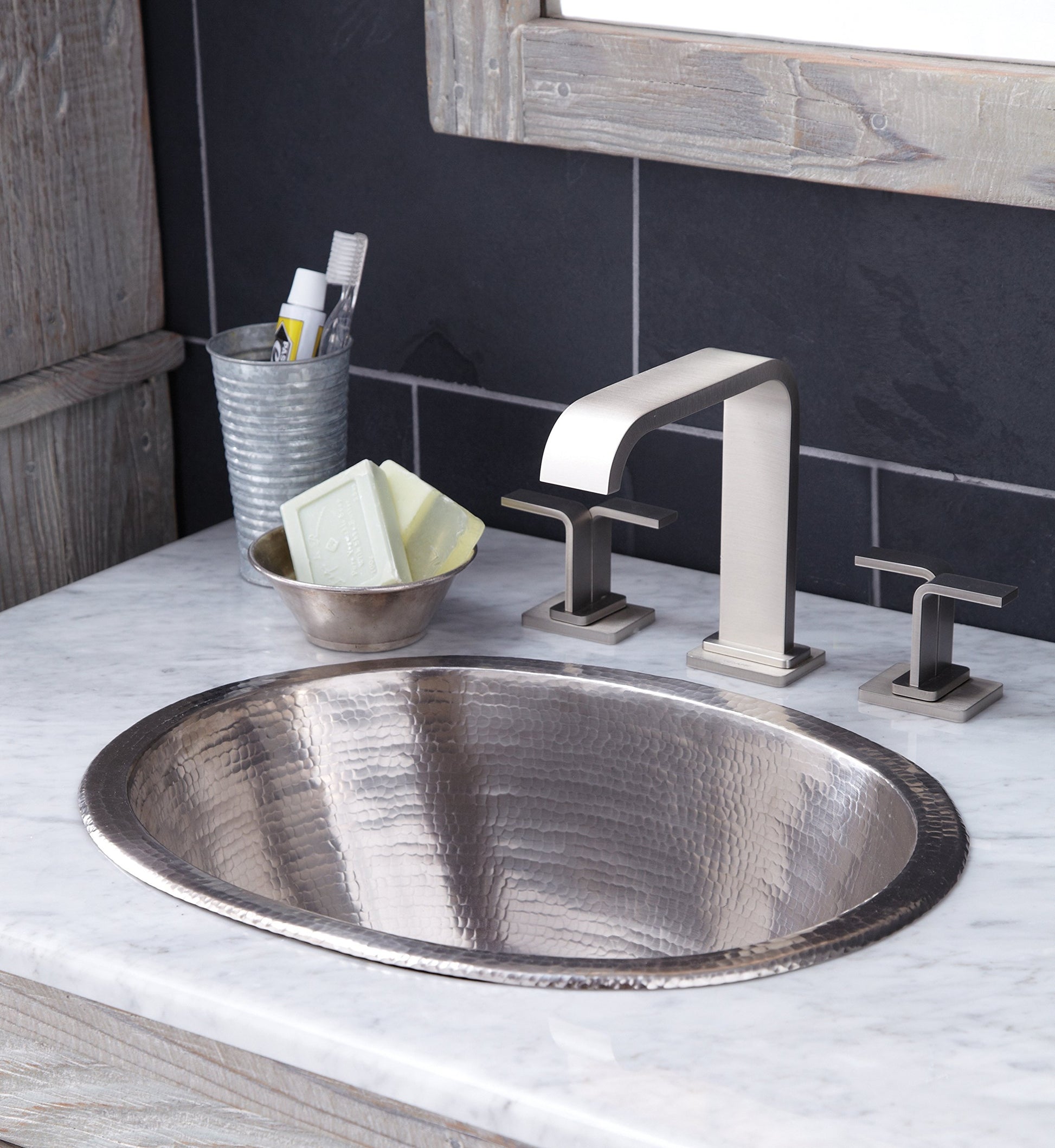 Oval hammered copper bathroom sink with textured surface installed in white marble countertop with chrome faucet.