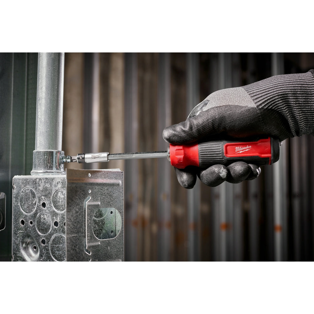 Red and black multi-bit screwdriver with extended bit being used on metal hardware, held in gloved hand.
