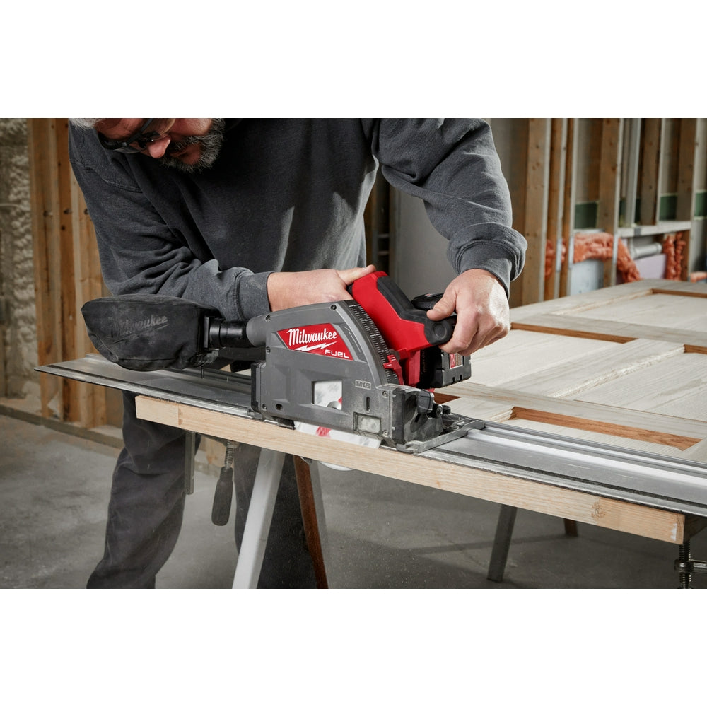Red and black Milwaukee circular saw with guide rail attached, held by person over wooden workpiece.