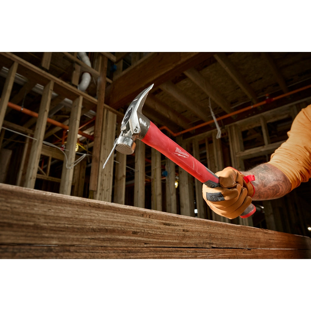 Claw hammer with metal head and red fiberglass handle held above wooden beam on construction site.