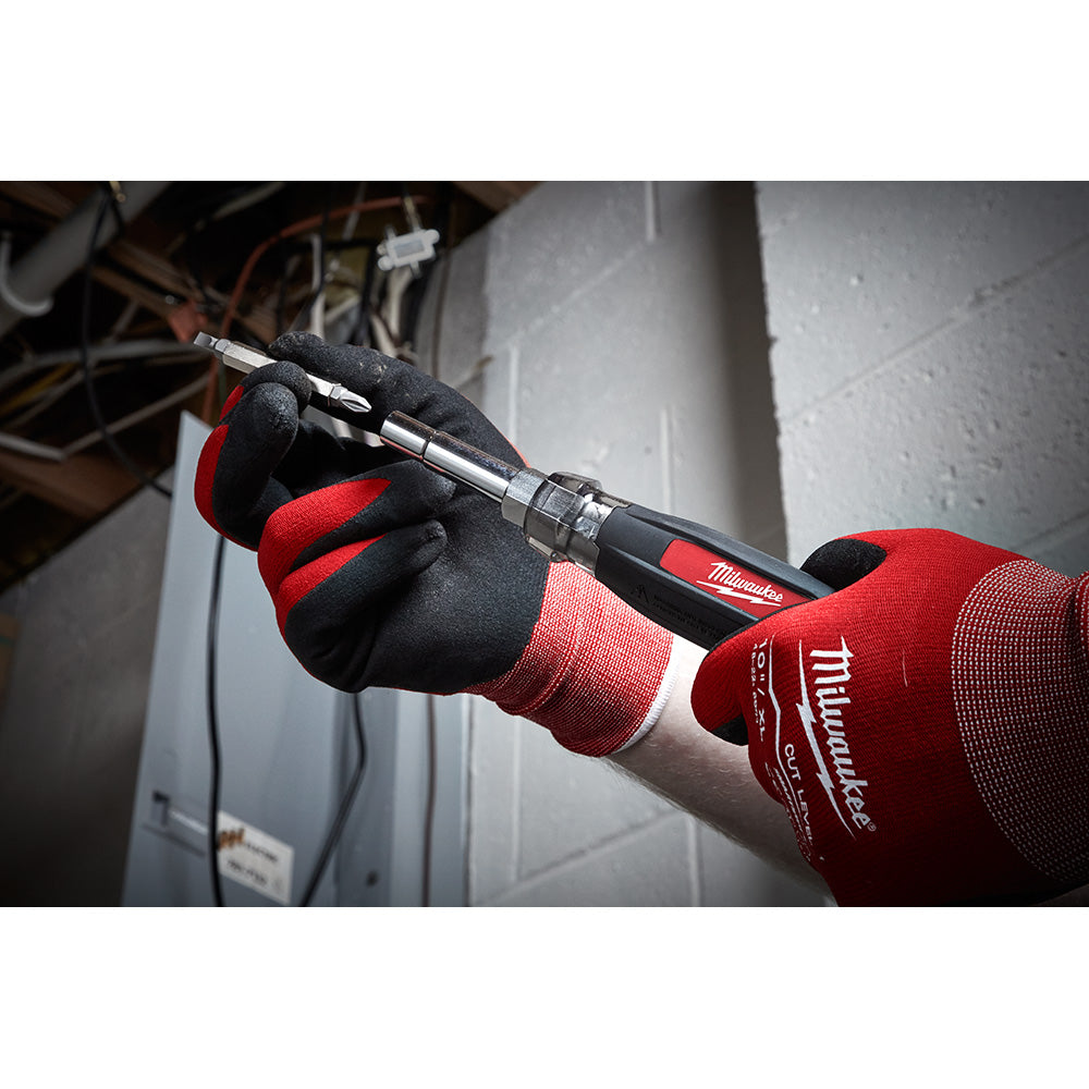 Milwaukee multi-bit screwdriver with cushioned grip held in a gloved hand, showing interchangeable bits and black handle with
