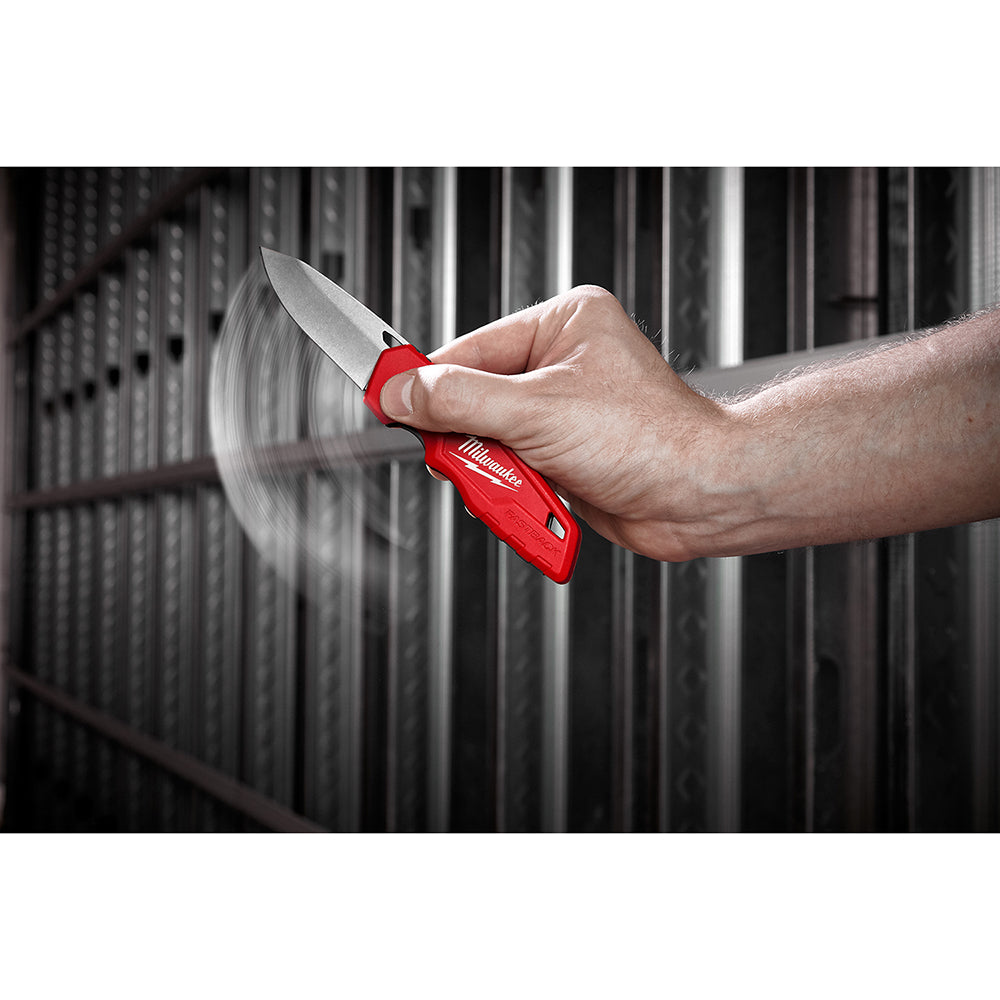 Red folding pocket knife with silver blade held open in a hand against a corrugated metal background.