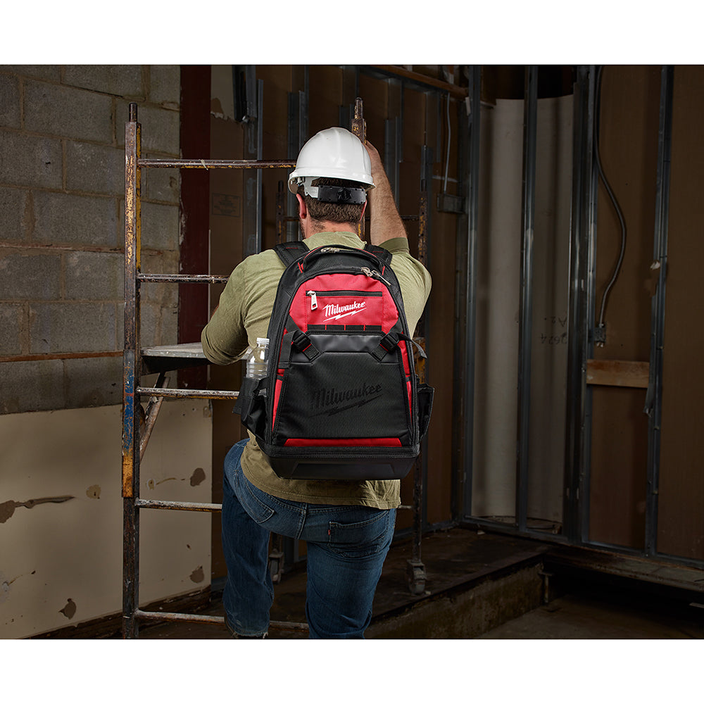 Black and red Milwaukee backpack worn by worker on jobsite, featuring multiple compartments and shoulder straps.