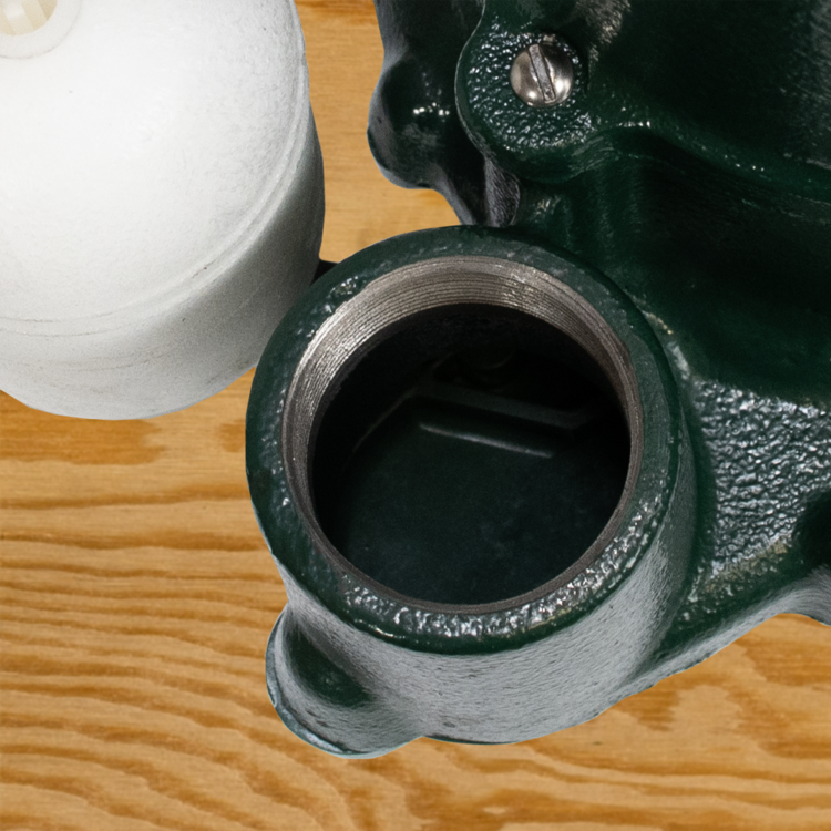 Green and gray cast iron sump pump with threaded outlet port and adjustment bolt, viewed from above on wood surface.