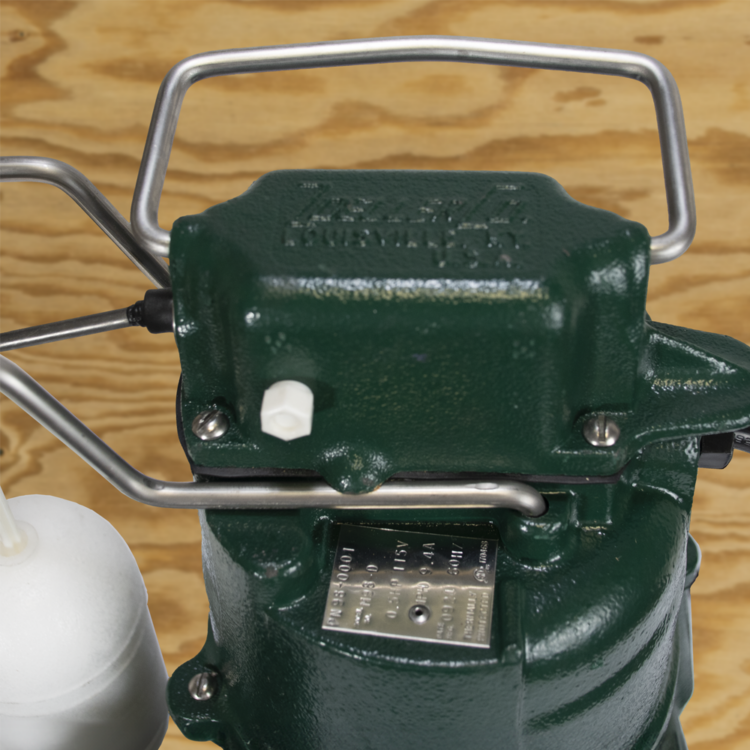 Green cast iron submersible sump pump with metal handle, electrical cord, and nameplate on wooden surface.