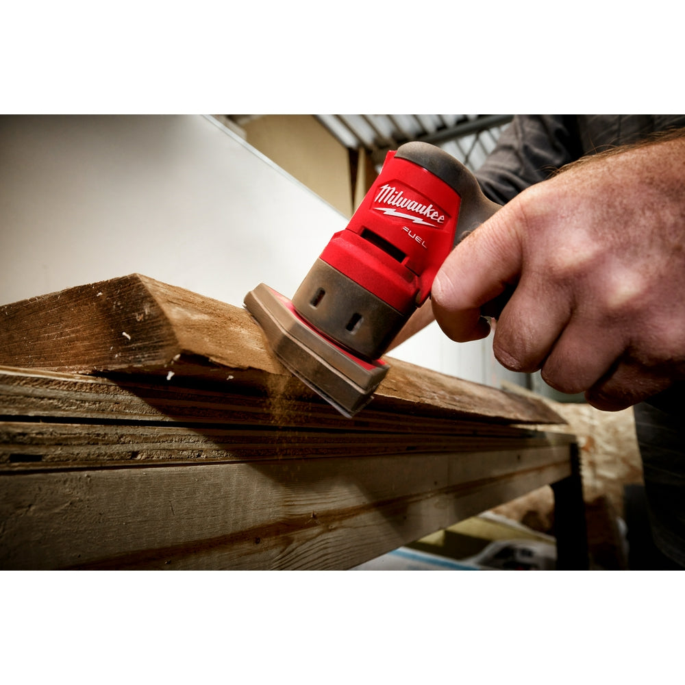 Red and black Milwaukee orbital sander with sponge interface pad being used on wooden surface.