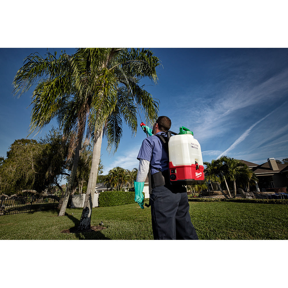 Person wearing backpack sprayer with red trigger wand extended upward in outdoor setting.