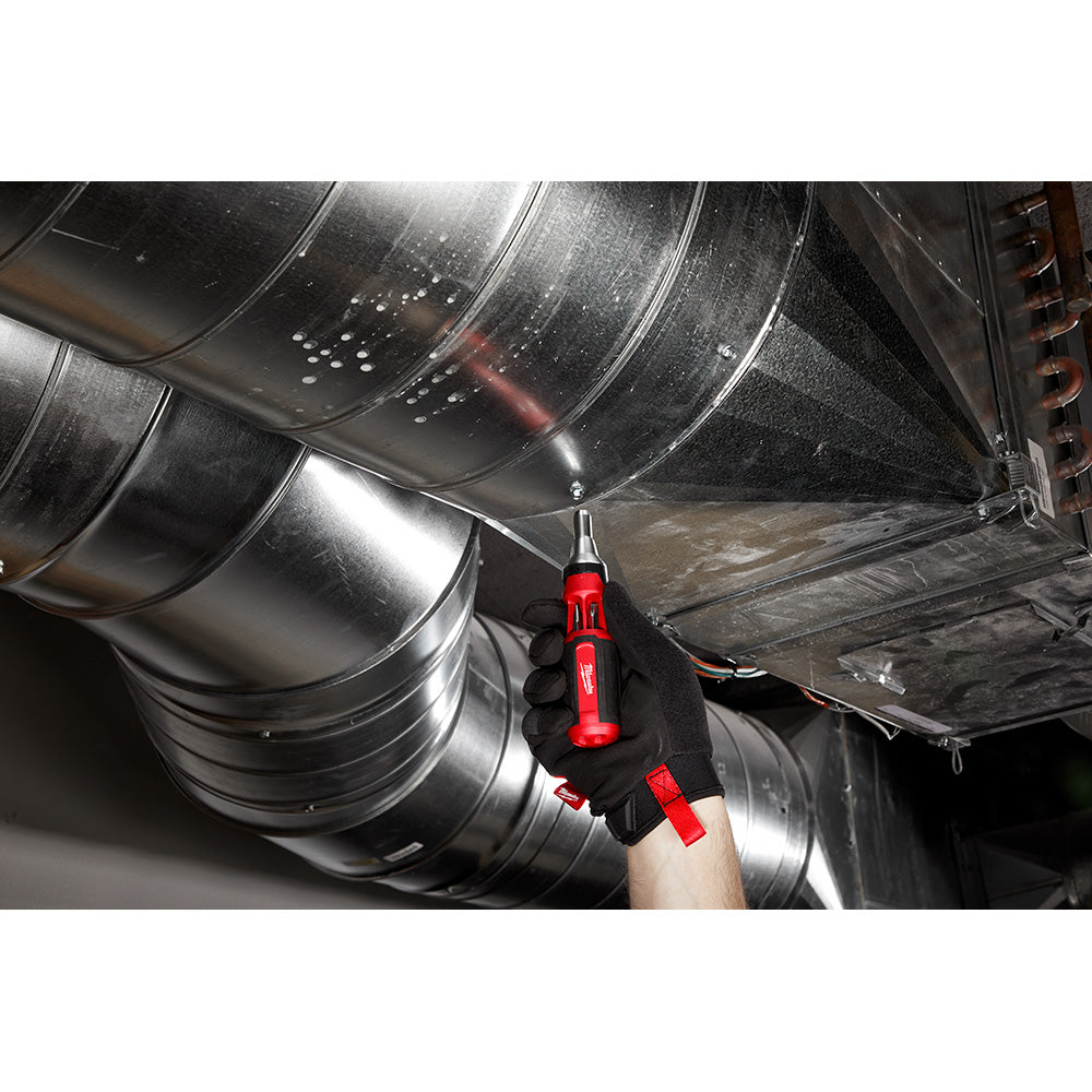 Red and black ratcheting multi-bit driver held in gloved hand against metal ductwork.