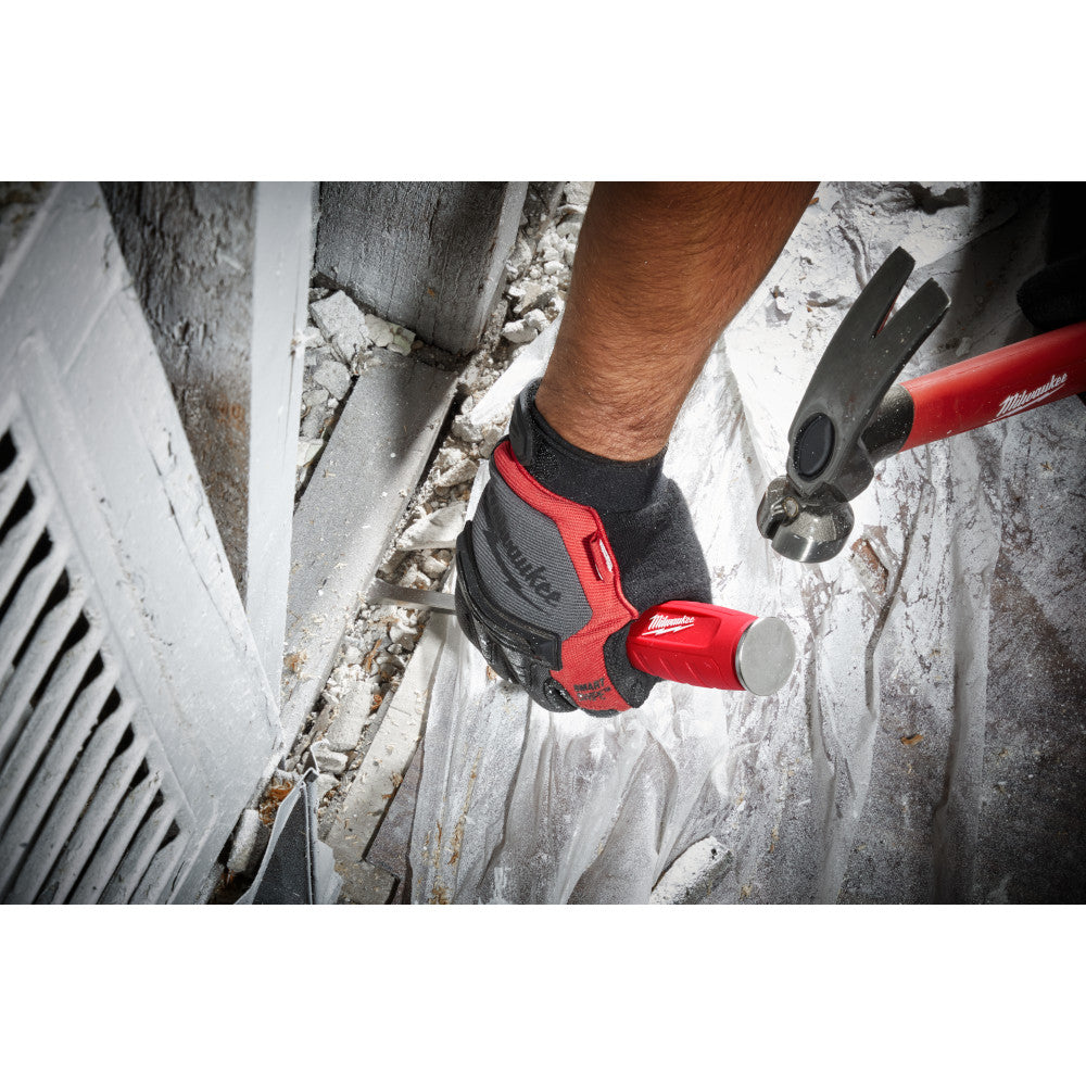 Hand wearing work gloves holding red and black demolition driver tool against concrete surface with debris.