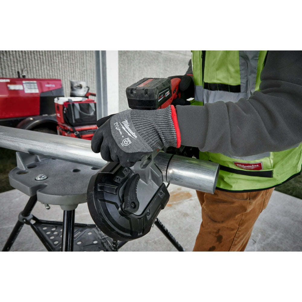 Black and gray work gloves with red accents being worn while holding a metal pipe in an industrial setting.