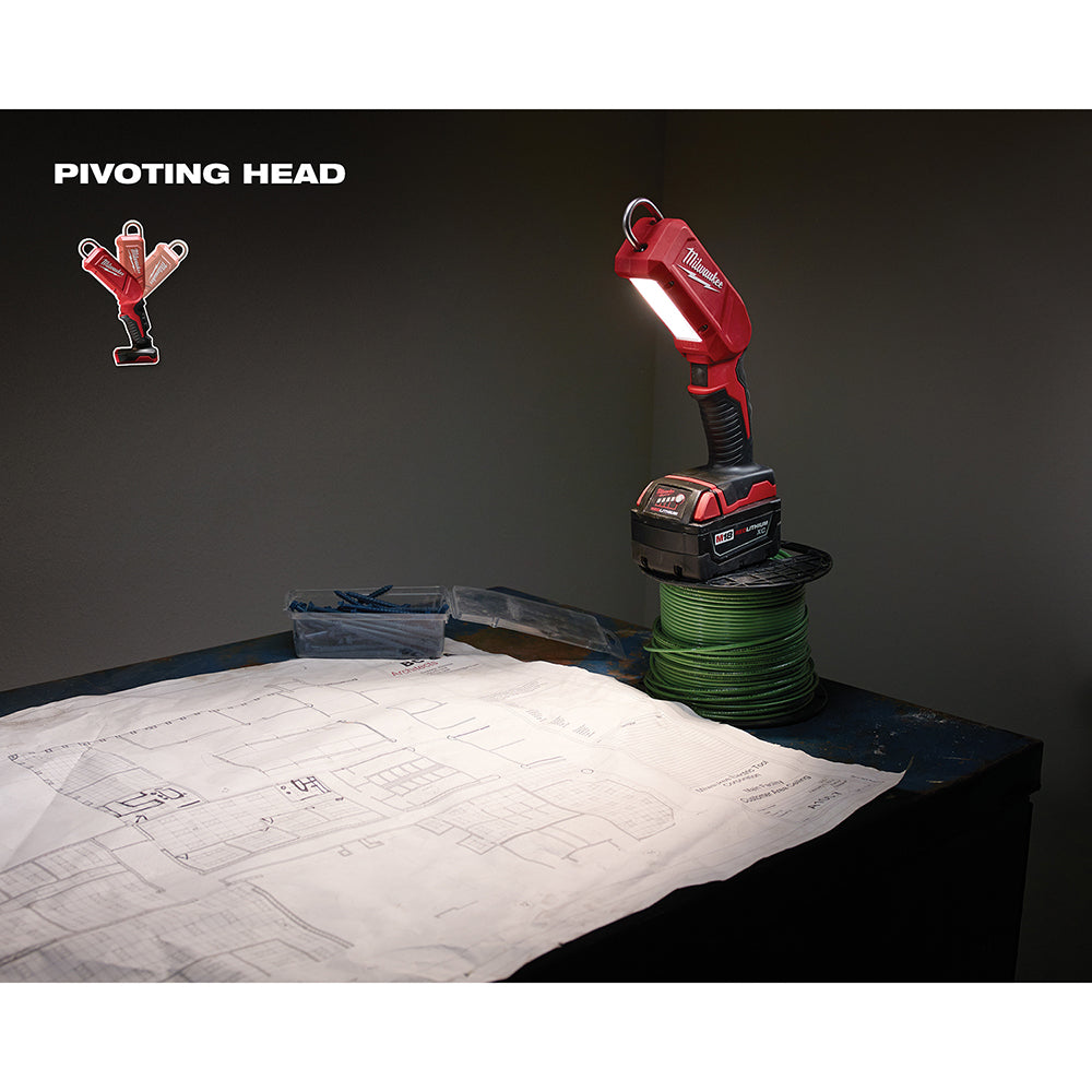 Red Milwaukee M18 LED stick light with pivoting head mounted on battery, illuminating work area over blueprints.