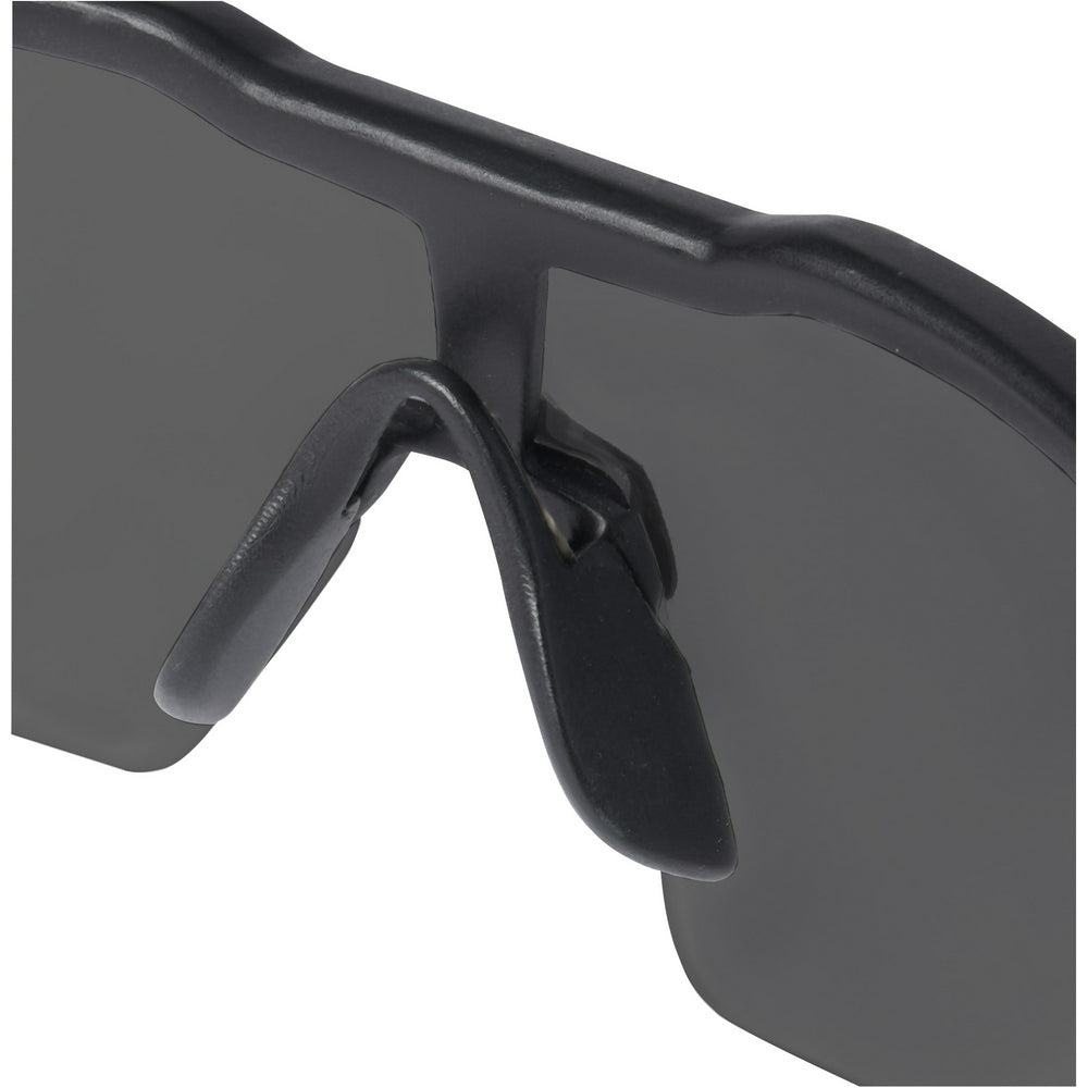 Black safety glasses with tinted gray lenses and adjustable nose bridge, angled side view.