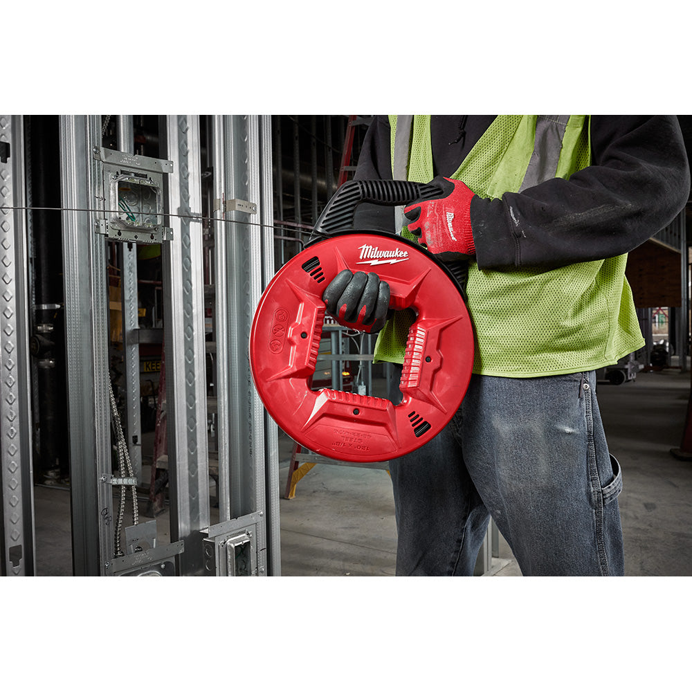 Red Milwaukee fish tape reel with steel cable being held by worker in safety vest near electrical panel.