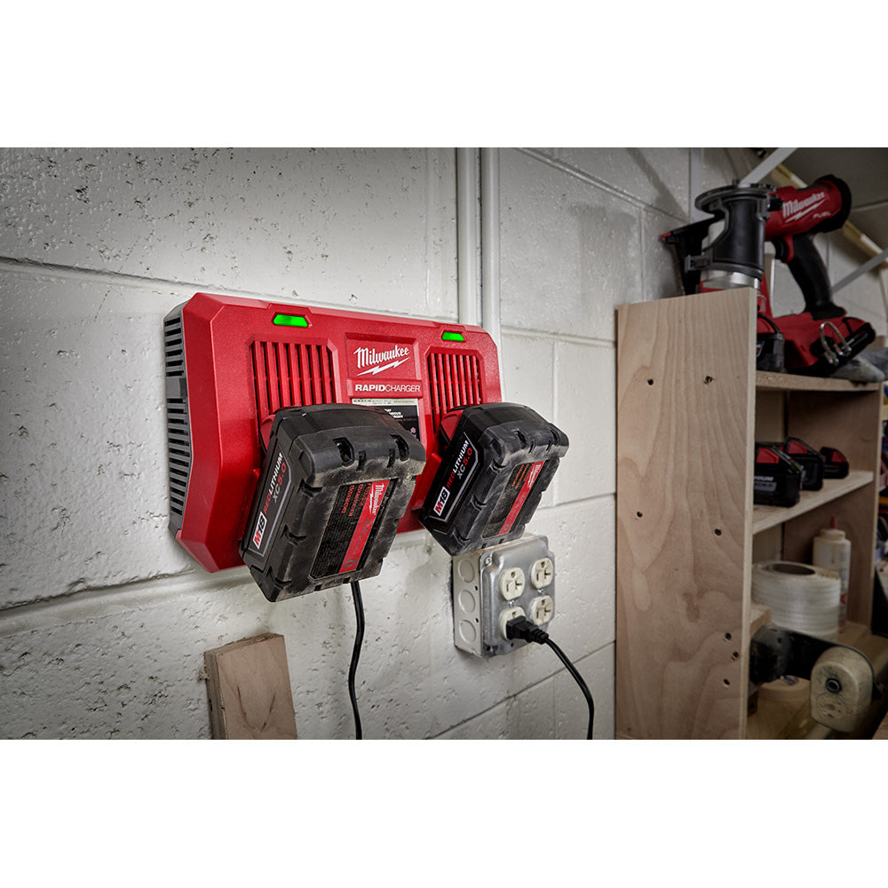 Red Milwaukee M18 dual bay charger mounted on wall with two black batteries installed in charging slots.