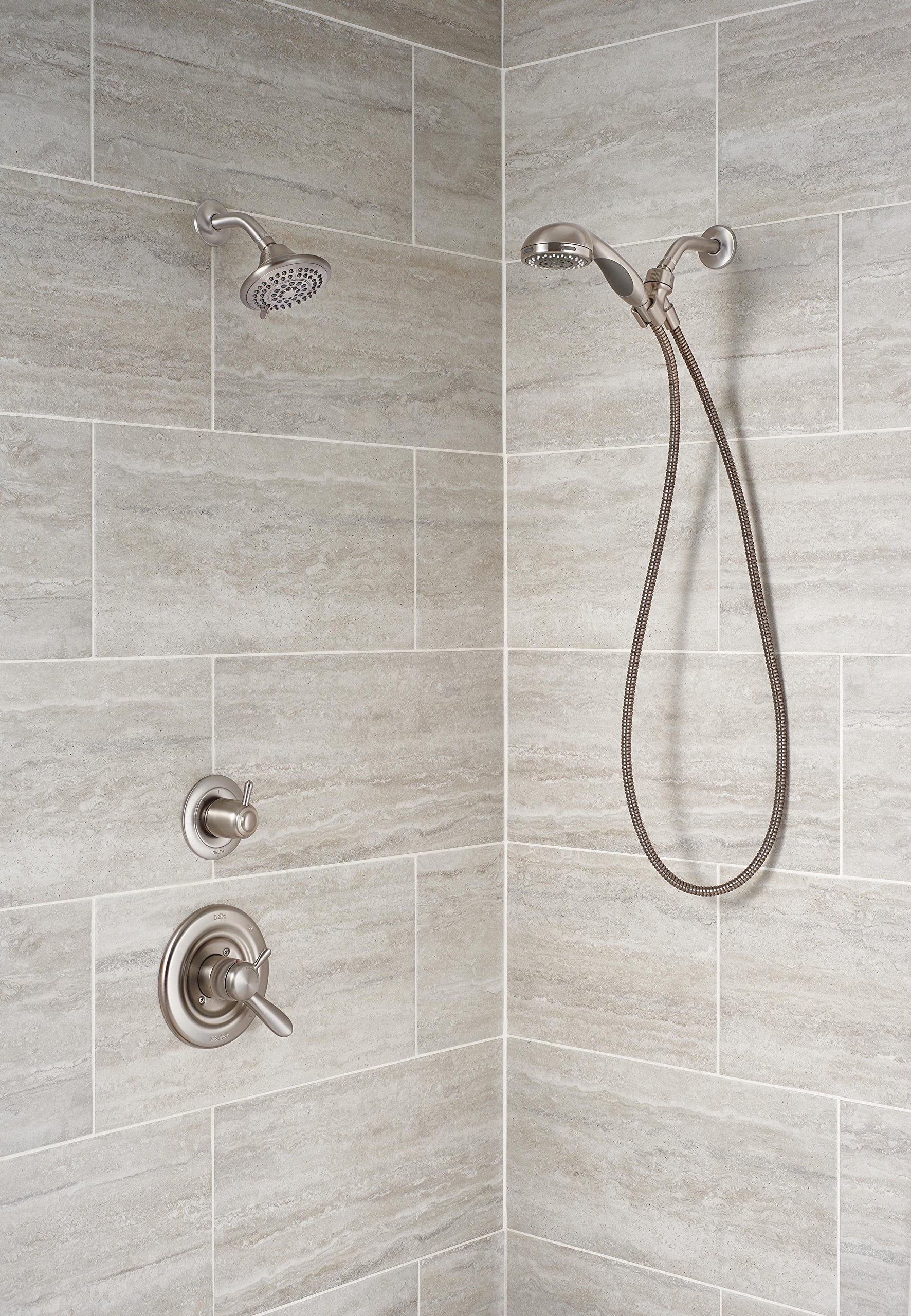 Stainless steel curved shower arm mounted on tiled bathroom wall with showerhead and handheld spray attachment.