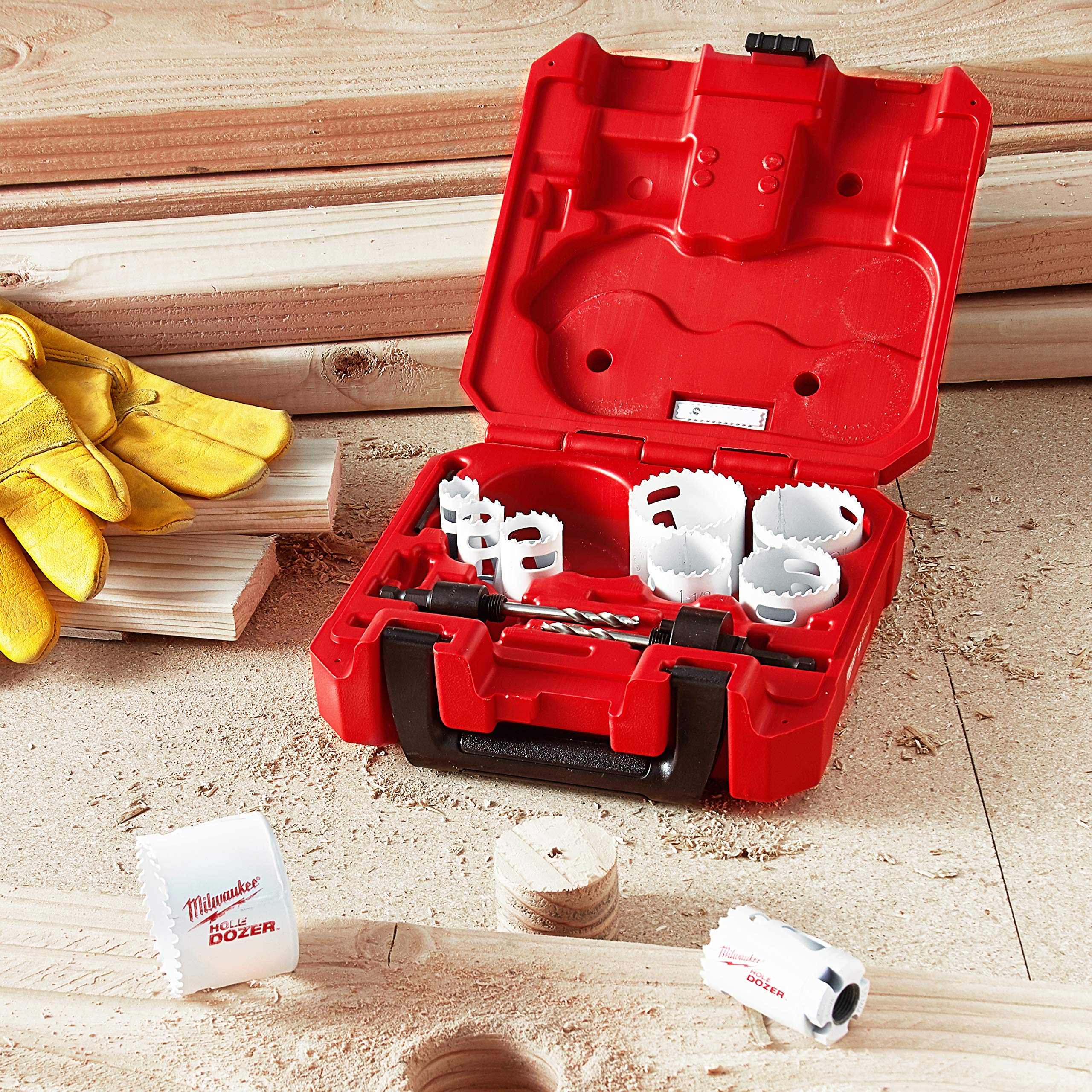 Red case containing white hole saw bits of varying sizes with drill arbor and accessories on wood surface.