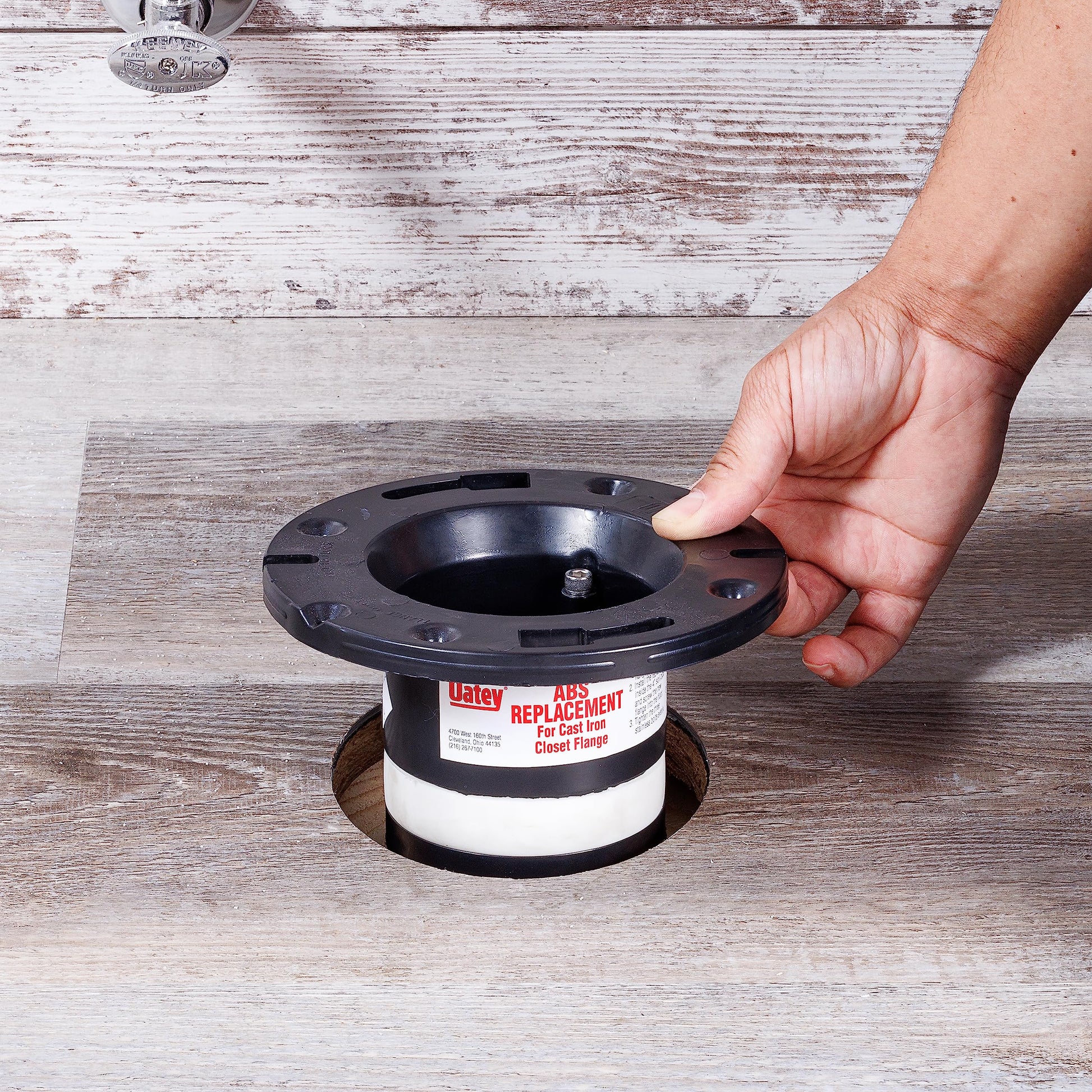 Black and white ABS closet flange with central opening, held by hand over wooden surface.