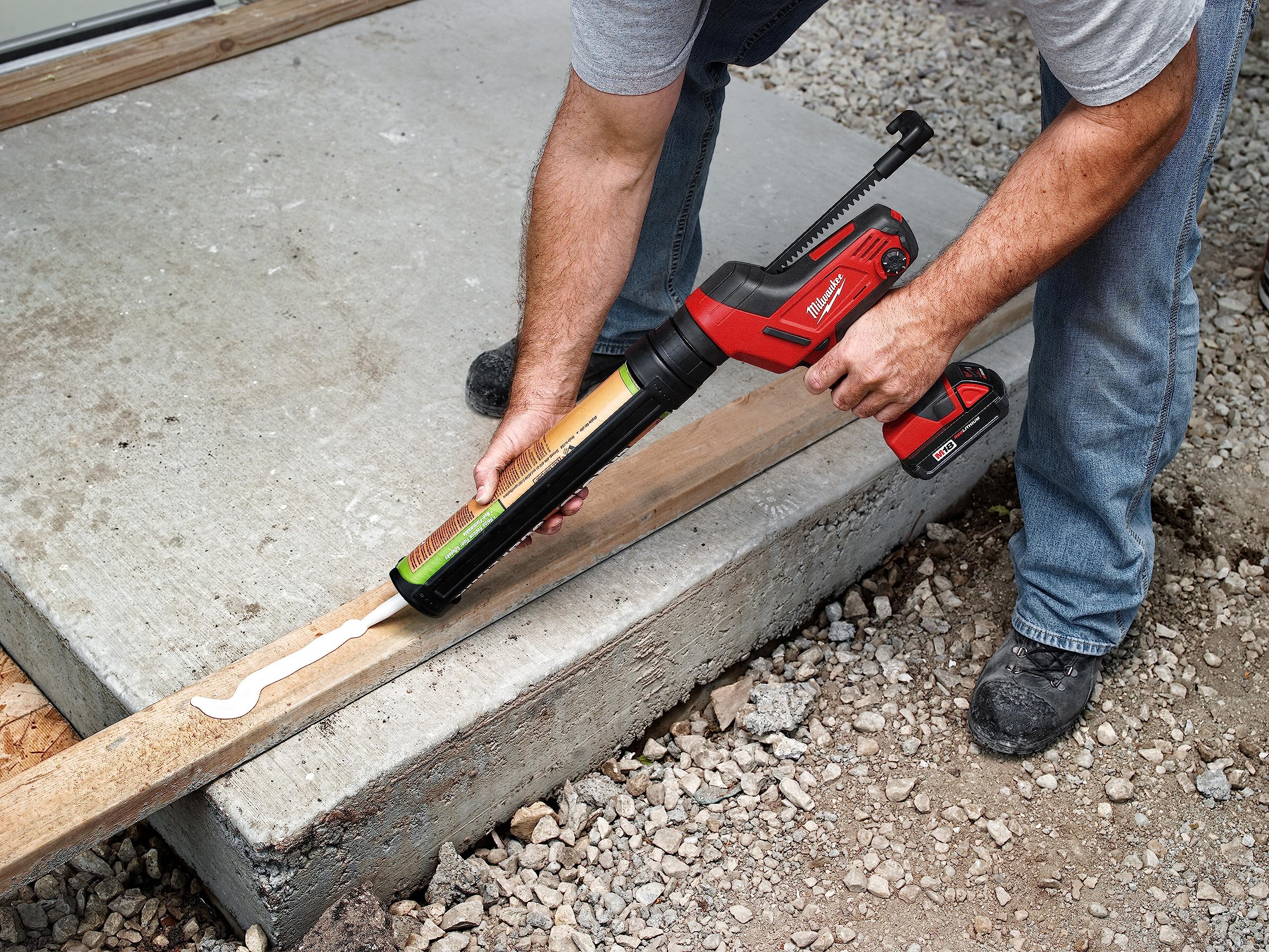 Person using red and black Milwaukee caulking gun with aluminum barrel on wooden trim joint.