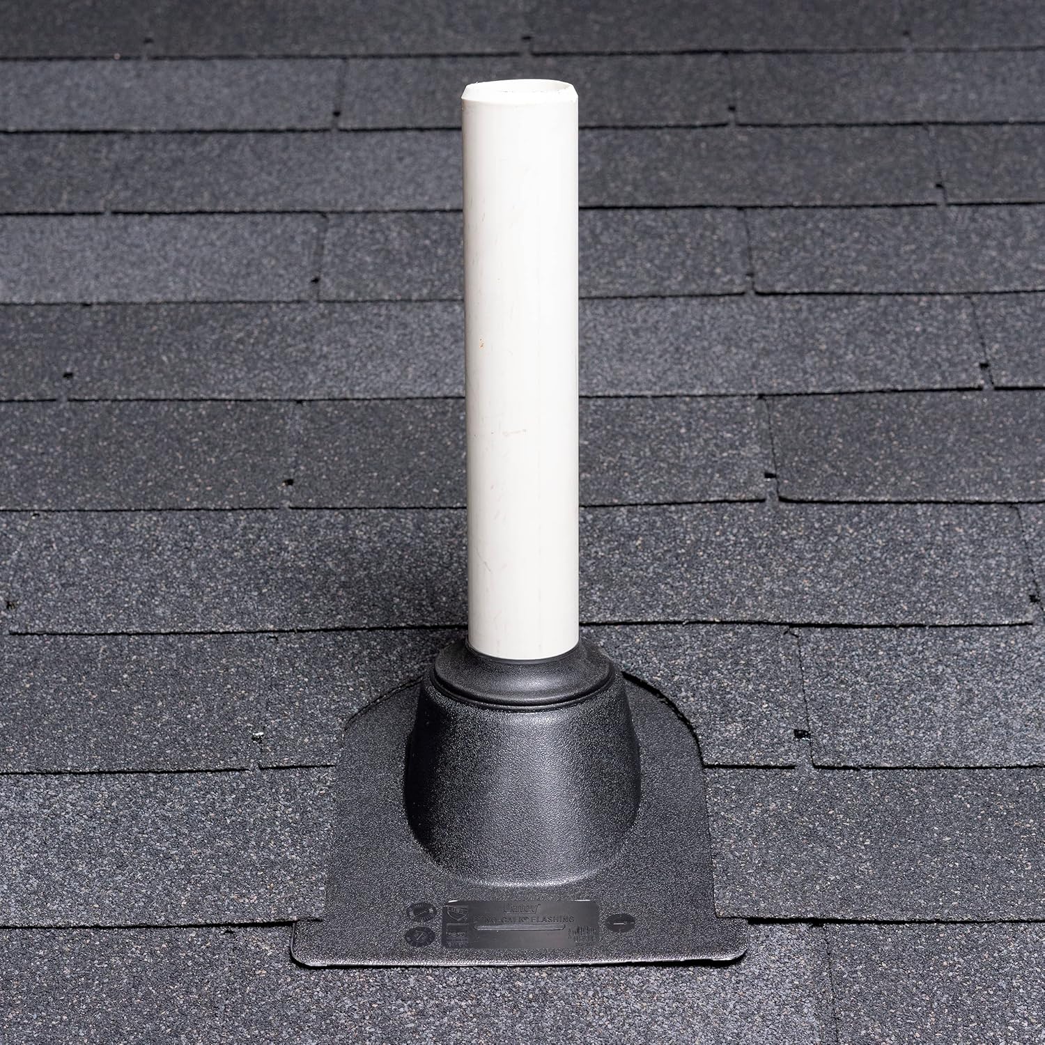 White plastic roof flashing with cylindrical pipe collar and rectangular base installed on asphalt shingle roof.