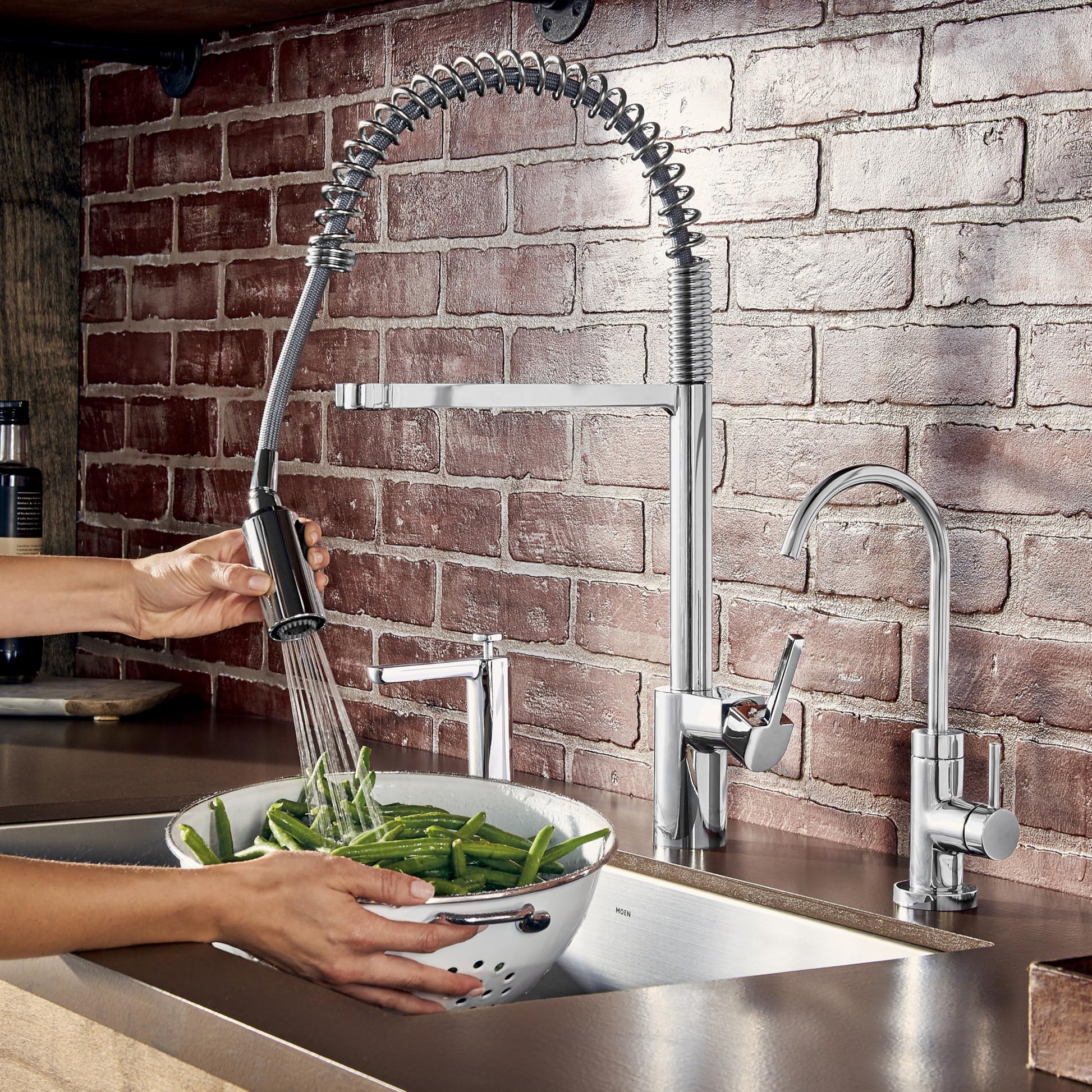 Chrome kitchen faucet with high arc spout and pulldown sprayer head being used to rinse vegetables in sink.