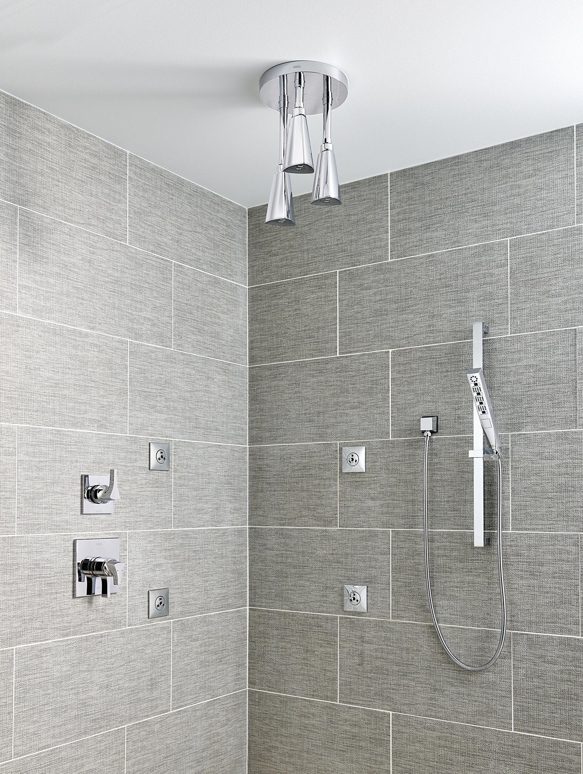 Chrome square wall elbow mounted on tiled bathroom wall, connecting to hand shower hose.