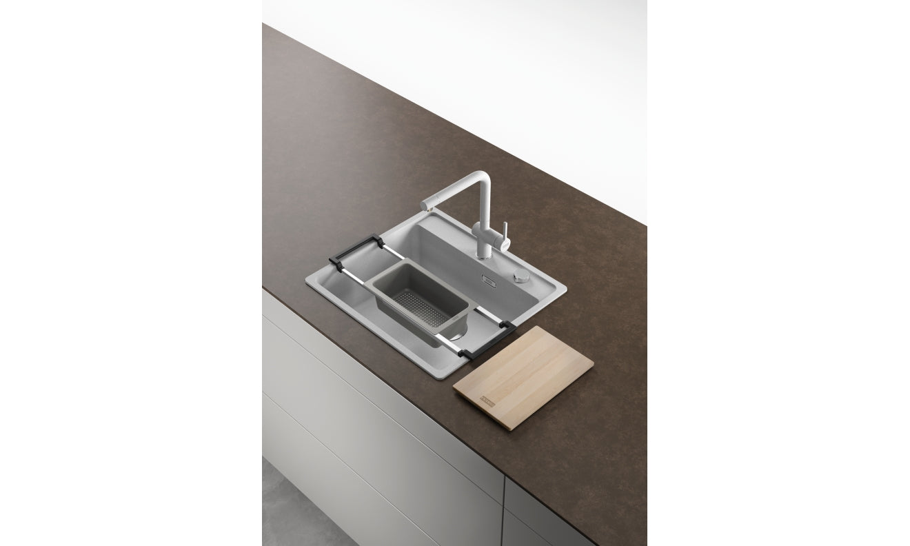 Stainless steel sink accessory system with white frame, multiple compartments, and wooden cutting board on dark countertop.