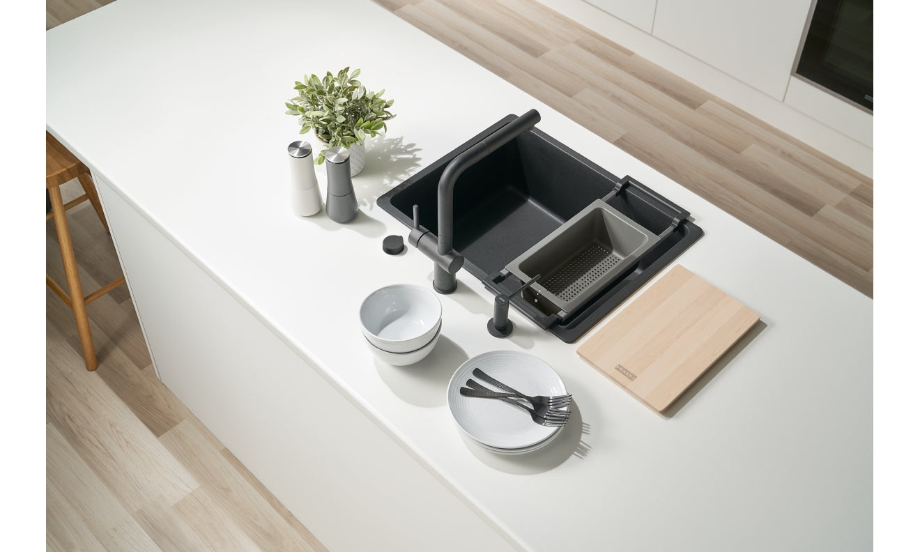 Black modular sink accessory system with removable baskets, strainers, and wooden cutting board displayed on white countertop