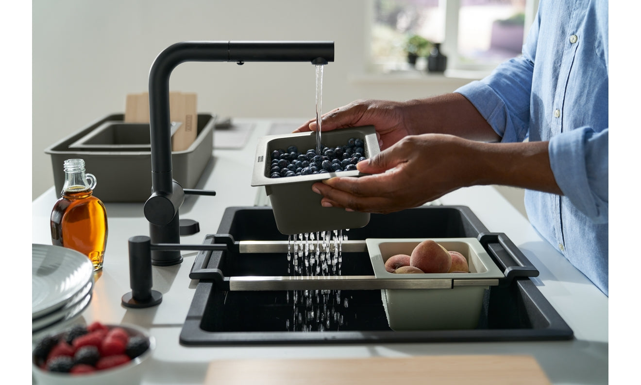 Black modular sink system with articulating faucet, rinsing blueberries in removable container over stainless steel basin.