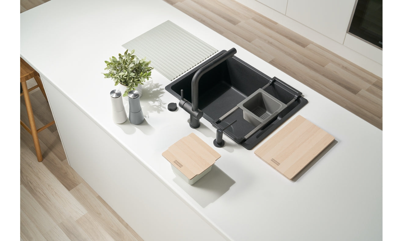 Black sink accessory system with multiple compartments, cutting boards, and integrated components displayed on white countert