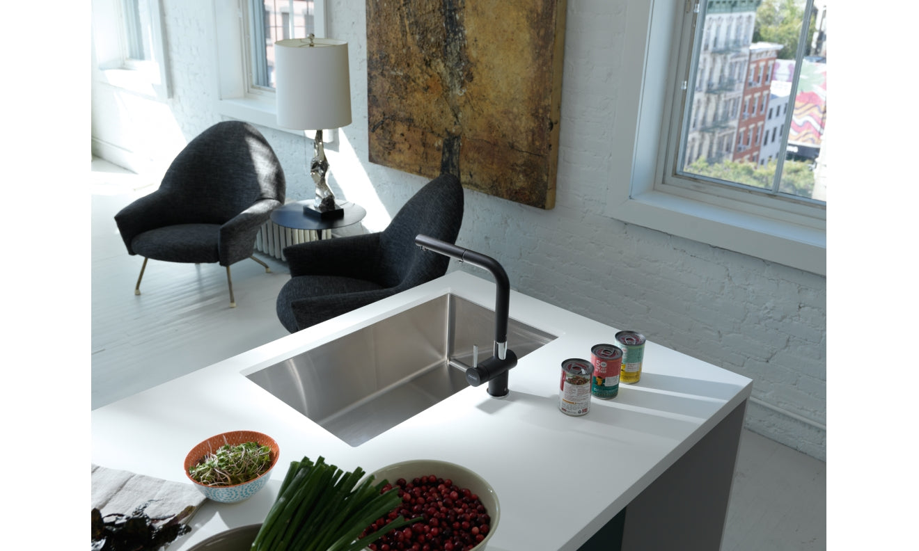 Stainless steel undermount sink with single bowl installed in white countertop with black faucet.