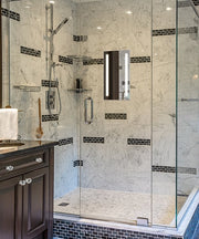 Rectangular fog-free mirror with dark frame mounted on marble shower wall above black subway tile accent strips.