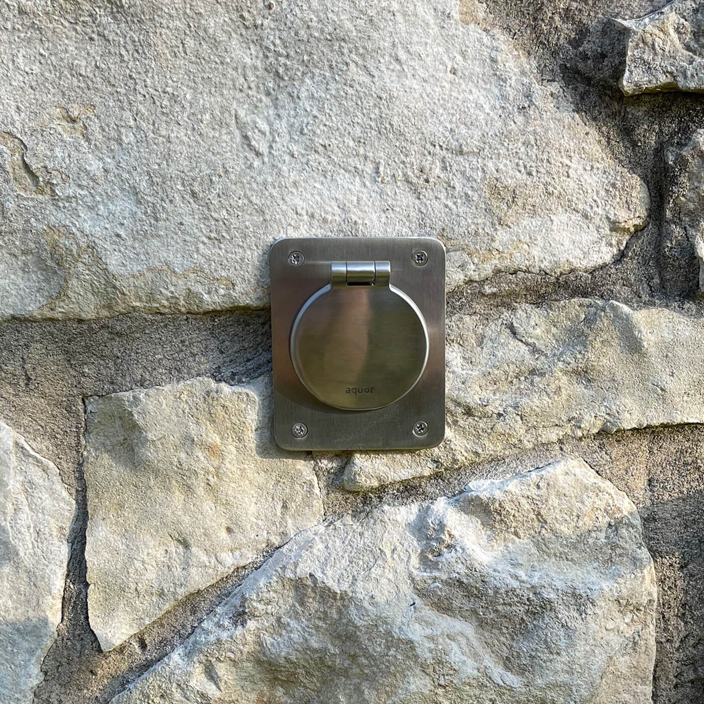 Stainless steel mounting plate with circular hinged component mounted on stone wall surface.