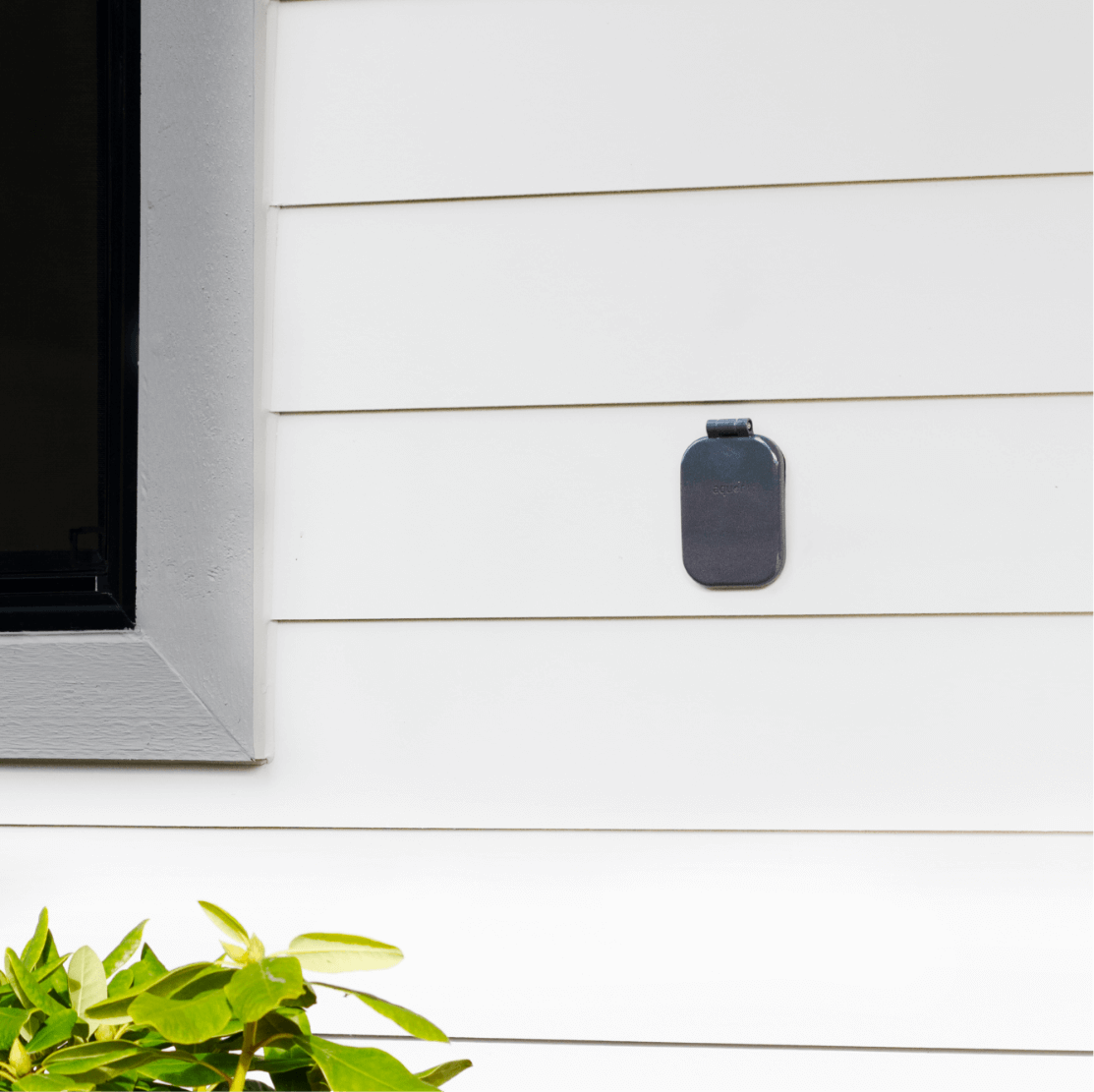 Slate grey house hydrant with hose connector mounted on white horizontal siding next to a window.