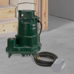 Green metal submersible pump with black cord and discharge hose on concrete surface.