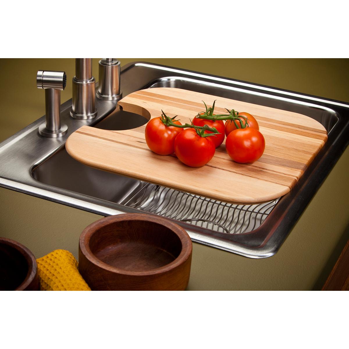 Light wood cutting board with rounded corners positioned over stainless steel sink, topped with fresh red tomatoes on the vin