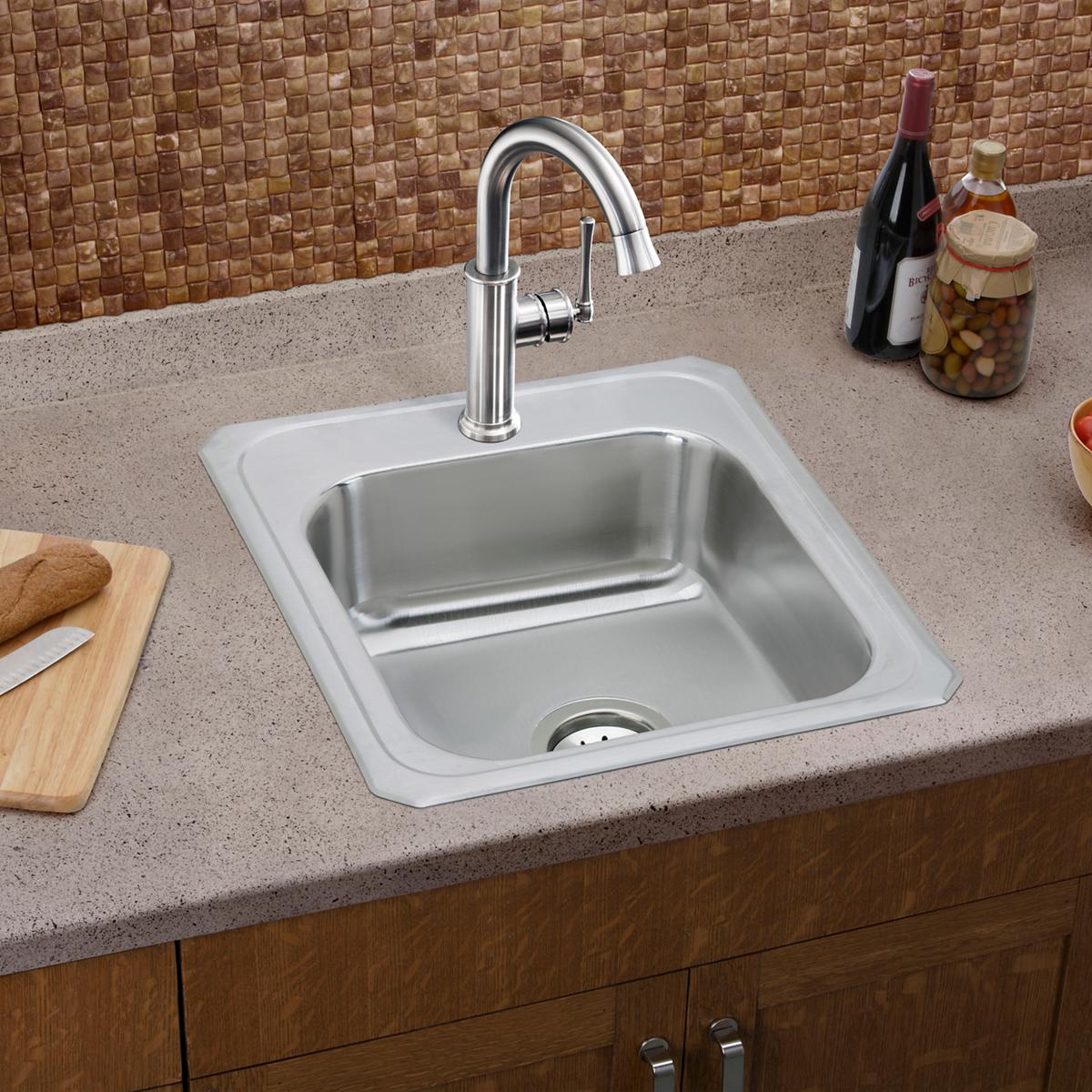 Stainless steel single bowl drop-in sink with white rim mounted in countertop, paired with chrome faucet.