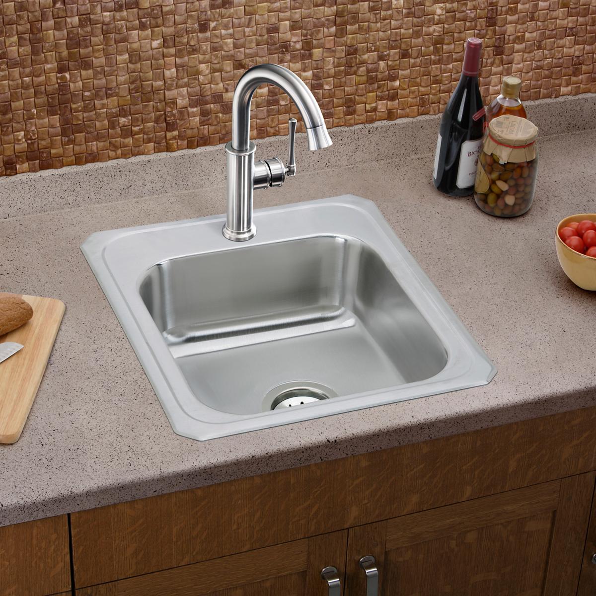 Lustrous steel single-hole bar faucet with forward lever handle mounted above stainless steel sink on countertop.