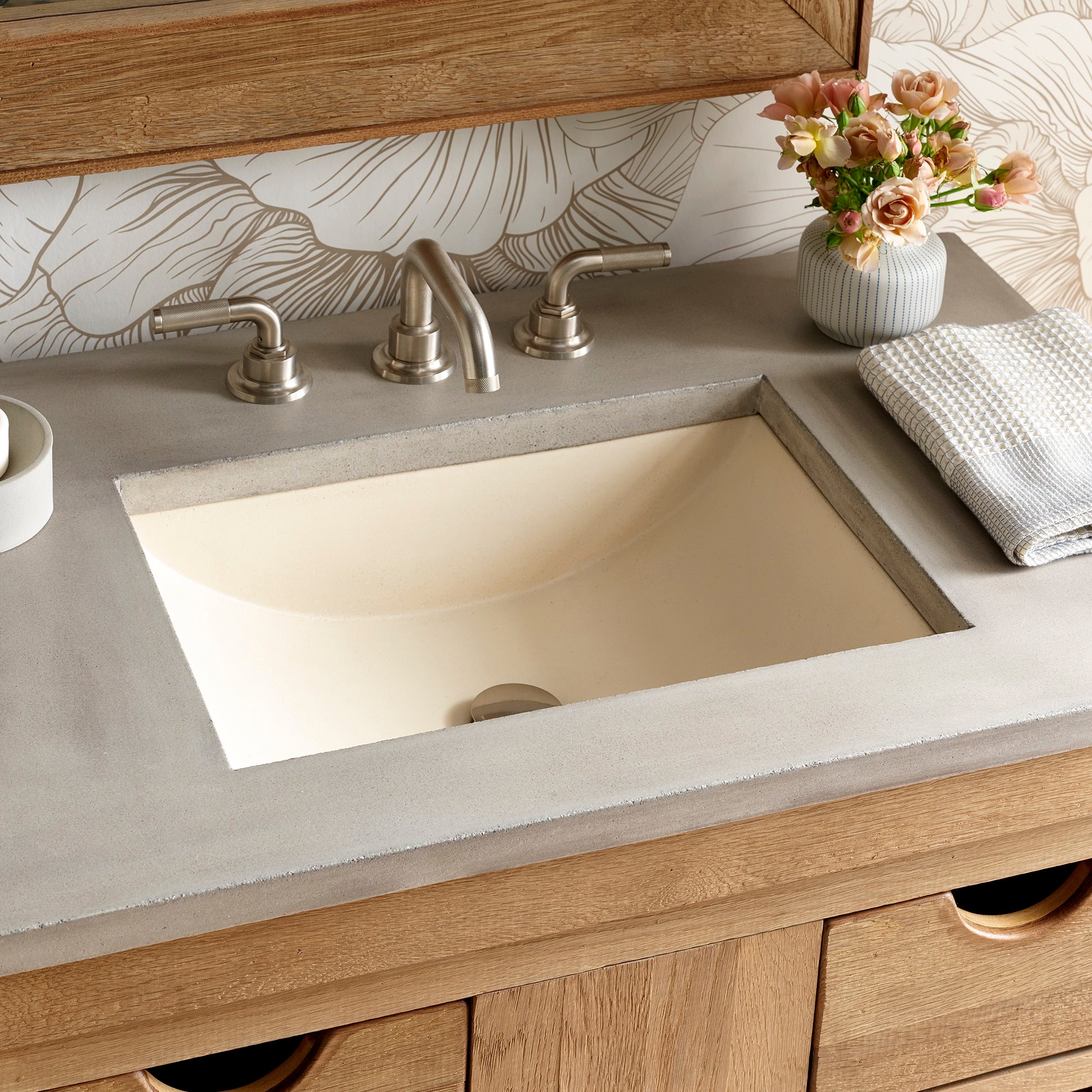 Undermount rectangular sink in cream with brushed nickel faucet on sand-colored countertop and wood vanity.